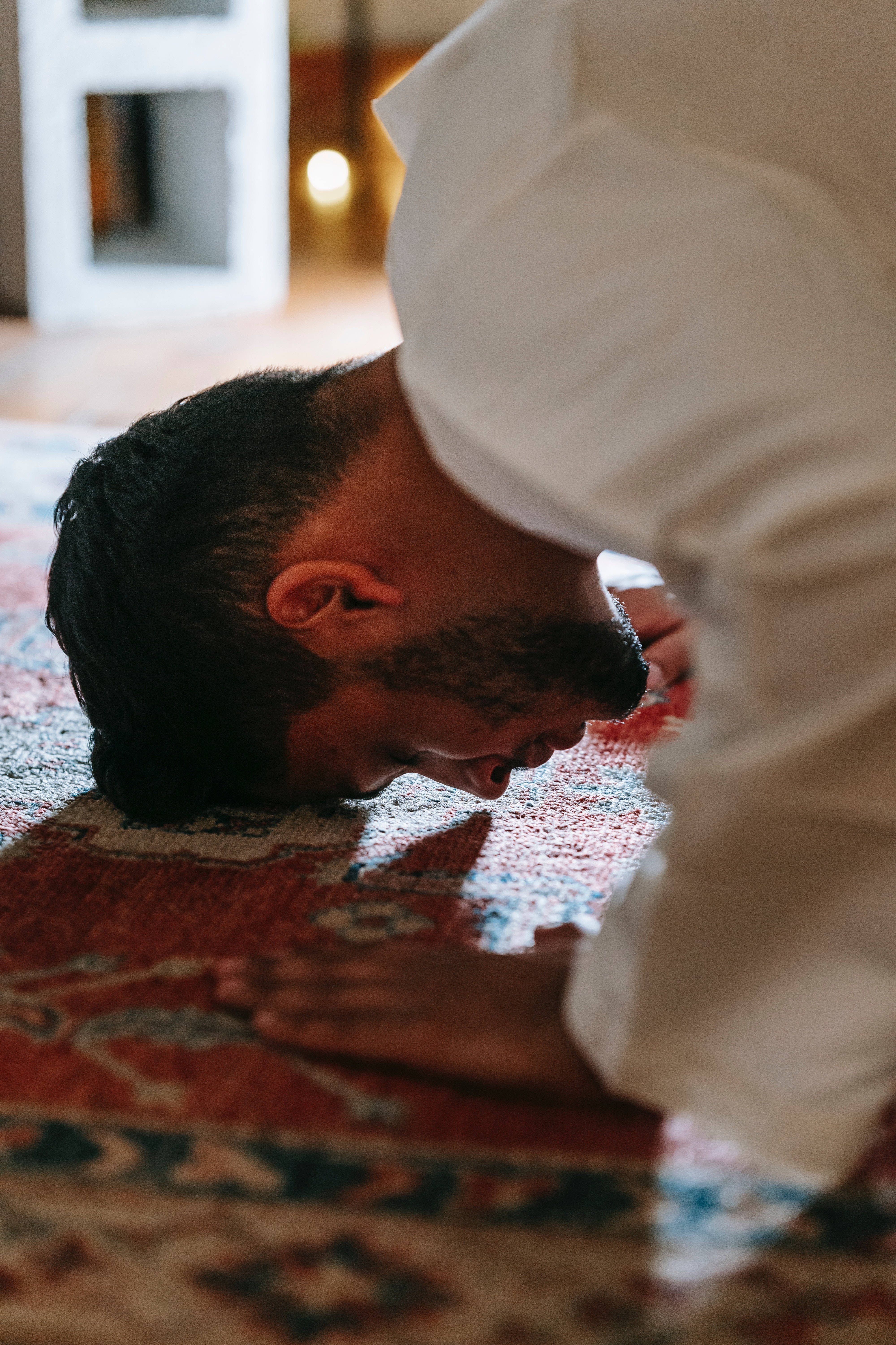 Best Islamic 桌布 壁紙 — 一名身穿白衣的男子在光線溫暖的室內空間中，跪伏在圖案地毯上。