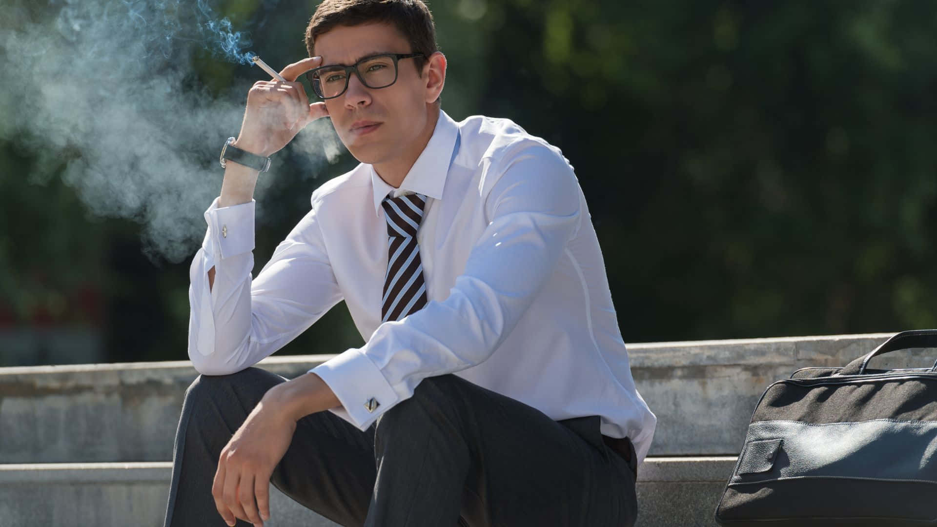 抽菸 桌布 壁紙 — 一名身穿白襯衫、戴眼鏡的年輕男子坐在戶外的混凝土台階上抽煙。