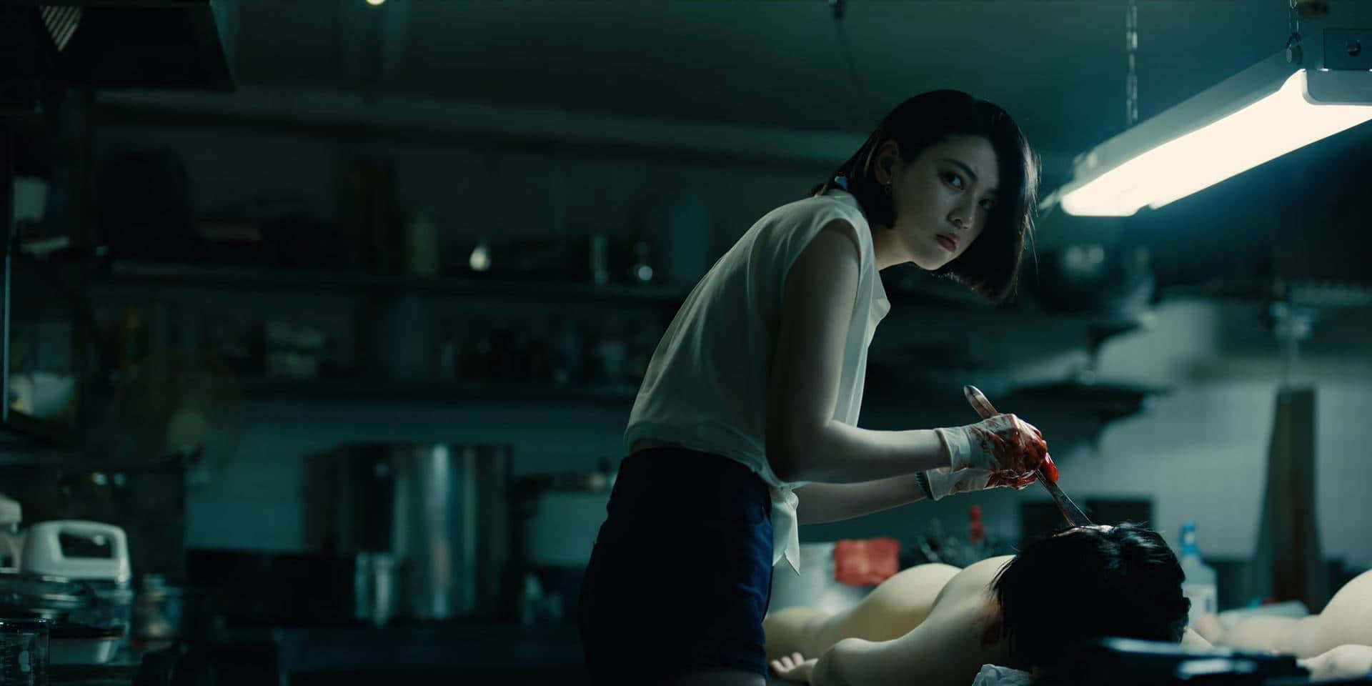 Alice In Borderland 桌布 壁紙 — 一名身穿白襯衫和手套的女子在昏暗雜亂的房間裡，在螢光燈下，手持一把血淋淋的刀，懸在一個俯臥的人上方。