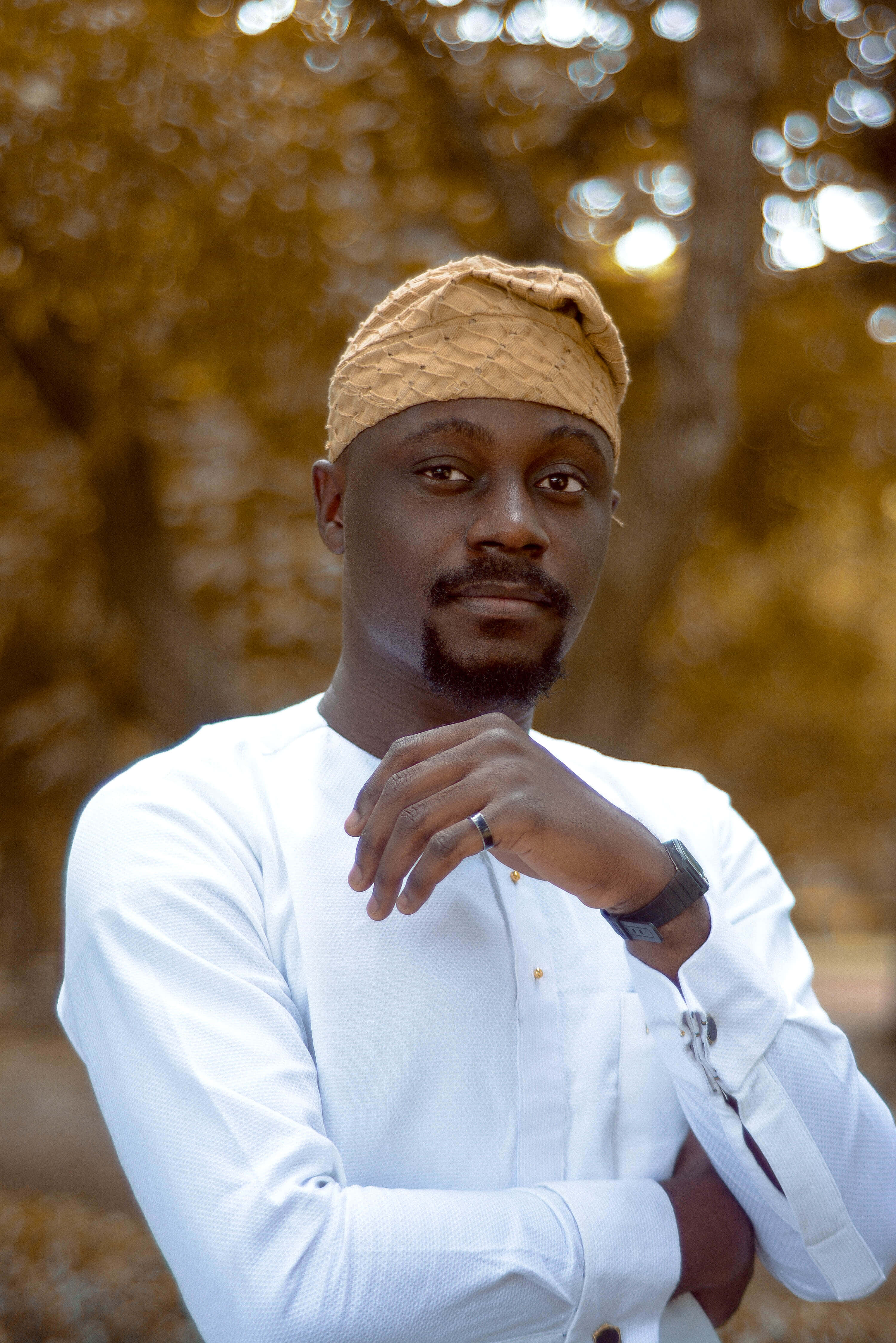 Nigeria 桌布 壁紙 — 一名身穿白襯衫和編織帽的男子自信地站在戶外，身後是模糊的金色樹葉。