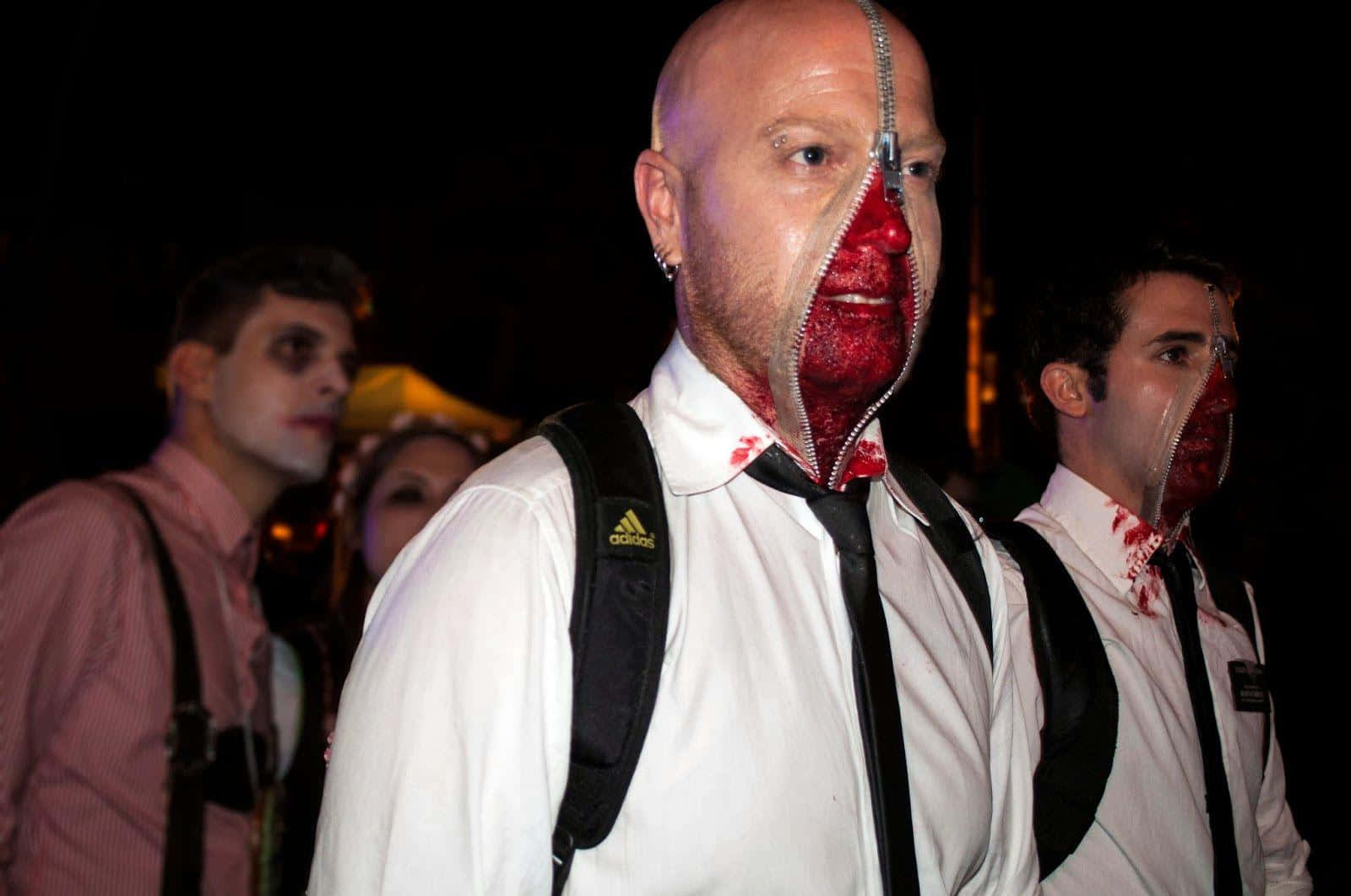 Horror Costumes 桌布 壁紙 — 一名身穿白襯衫打領帶的男子，臉部被拉鍊拉開，在戲劇性的夜間燈光下露出紅色的肉和血。