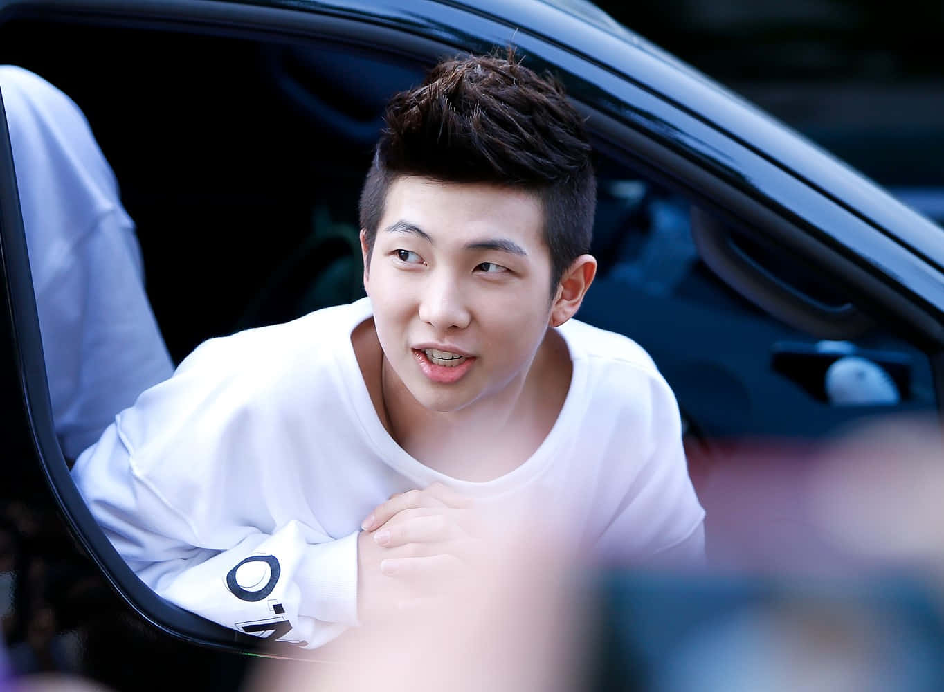 Bts Rap Monster 桌布 壁紙 — 一名身穿白襯衫的年輕男子，帶著頑皮的表情從車窗探出頭來。