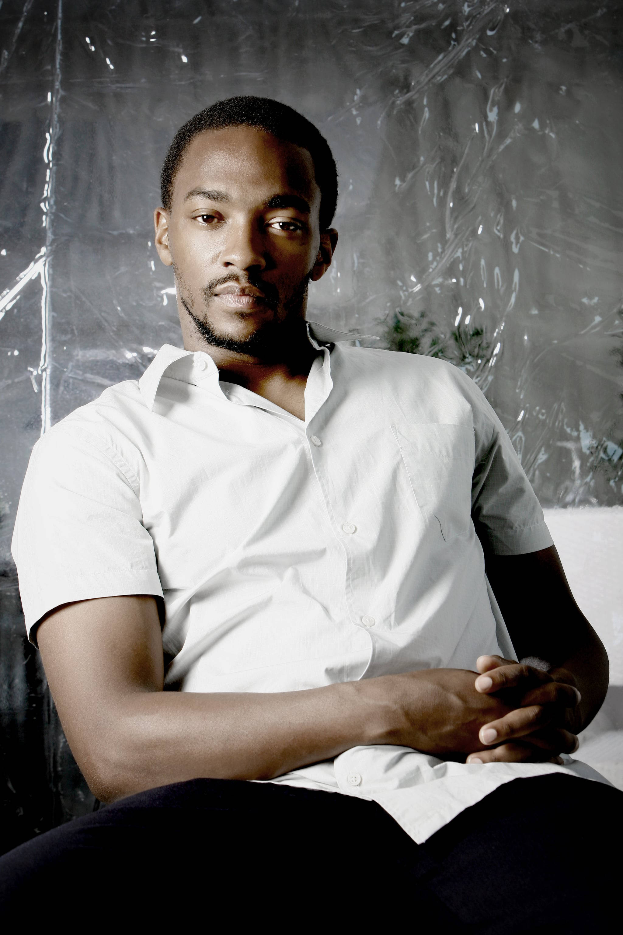 Anthony Mackie 桌布 壁紙 — 一名身穿白襯衫的男子，在帶有細微綠意的紋理灰色背景前平靜地坐著。