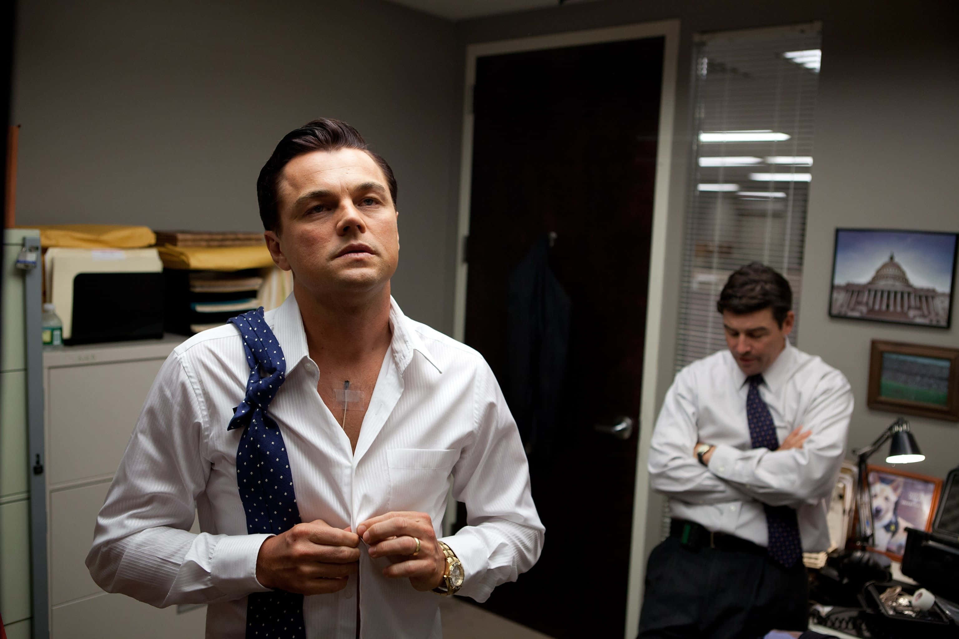 Wolf Of Wall Street 桌布 壁紙 — 一名身穿白襯衫的男子正在扣鈕，另一名男子雙手交叉站立在辦公室背景中。