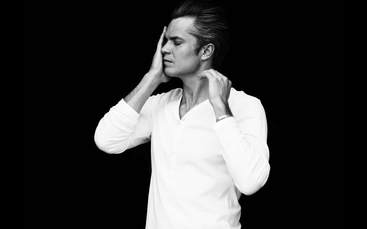 timothy olyphant 桌布 壁紙 — 一名身穿白襯衫的男子站在黑色背景前，雙手靠近臉部，擺出沉思的姿勢。