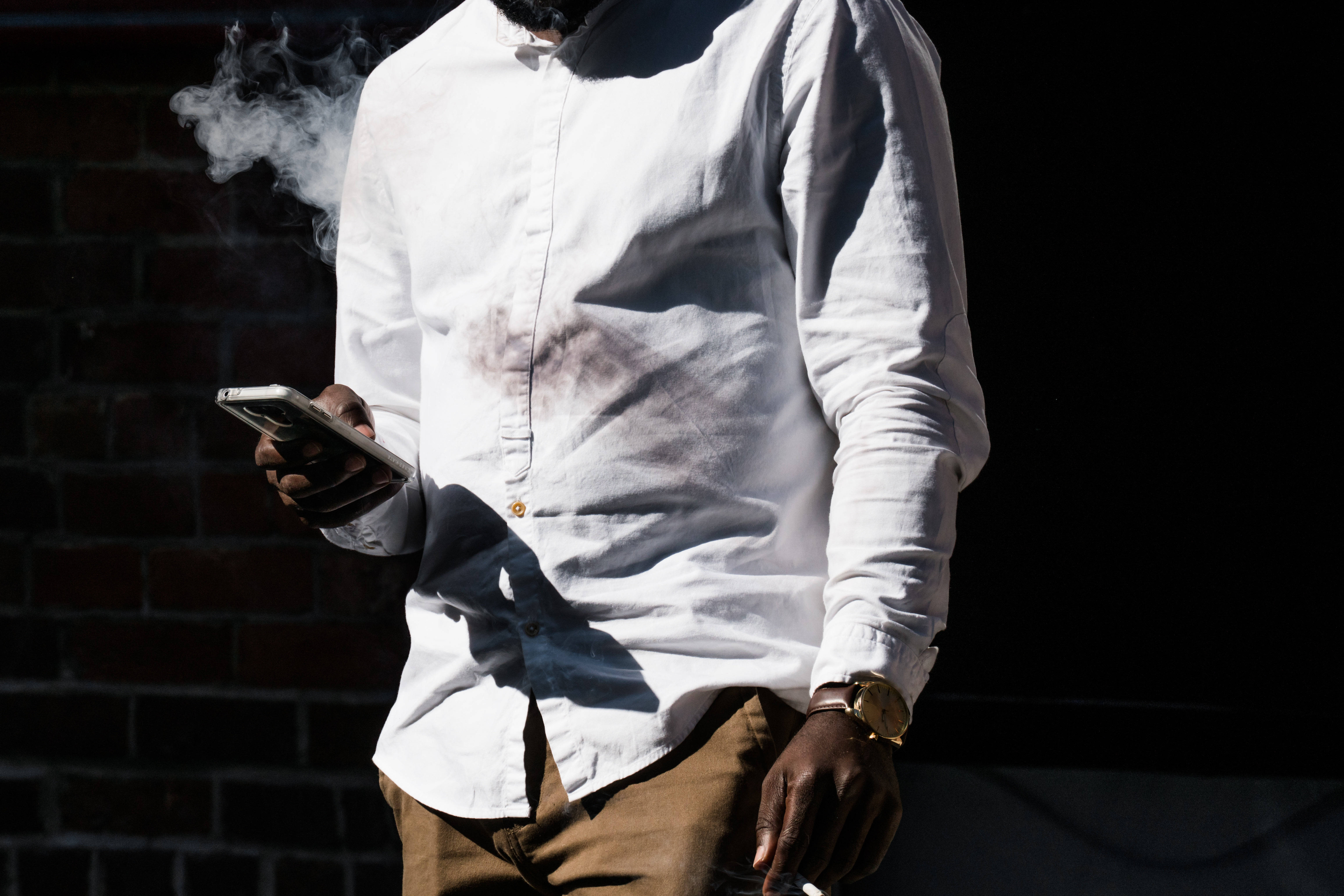 Smoking 桌布 壁紙 — 一名身穿白襯衫的男子靠著磚牆吸煙，同時手持智慧型手機。