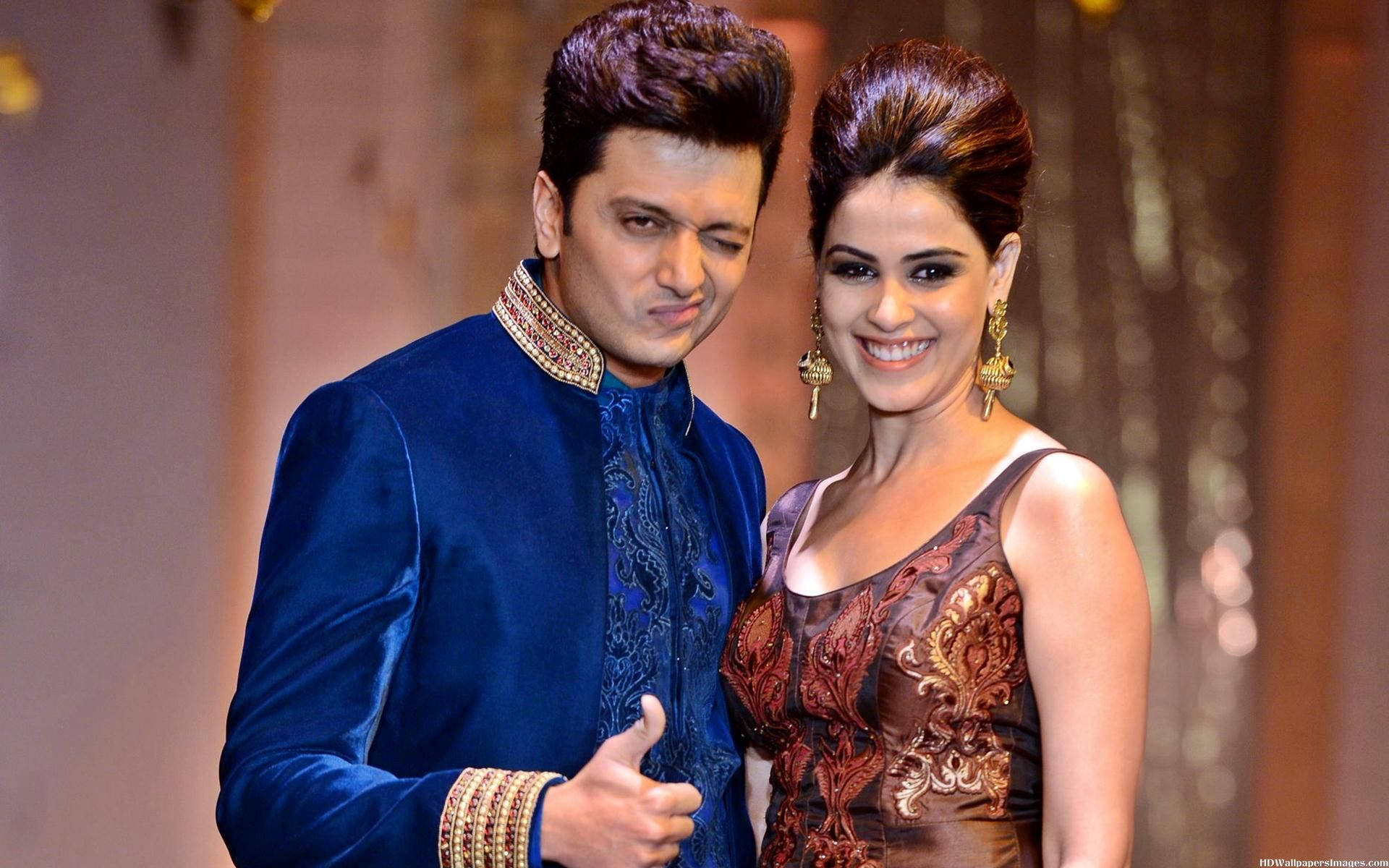 riteish deshmukh 桌布 壁紙 — 一名身穿皇家藍色天鵝絨 Sherwani 的男子和一名身穿棕色刺繡長袍的女子在一個華麗的活動中一起微笑。