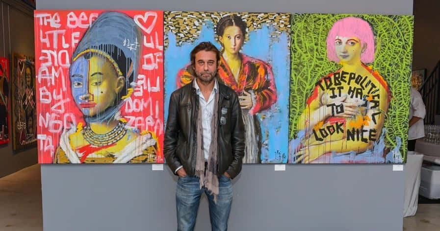 Jordi Mollà 桌布 壁紙 — 一名身穿皮夾克的男子站在畫廊中三幅充滿活力、充滿文字的普普藝術畫作前。