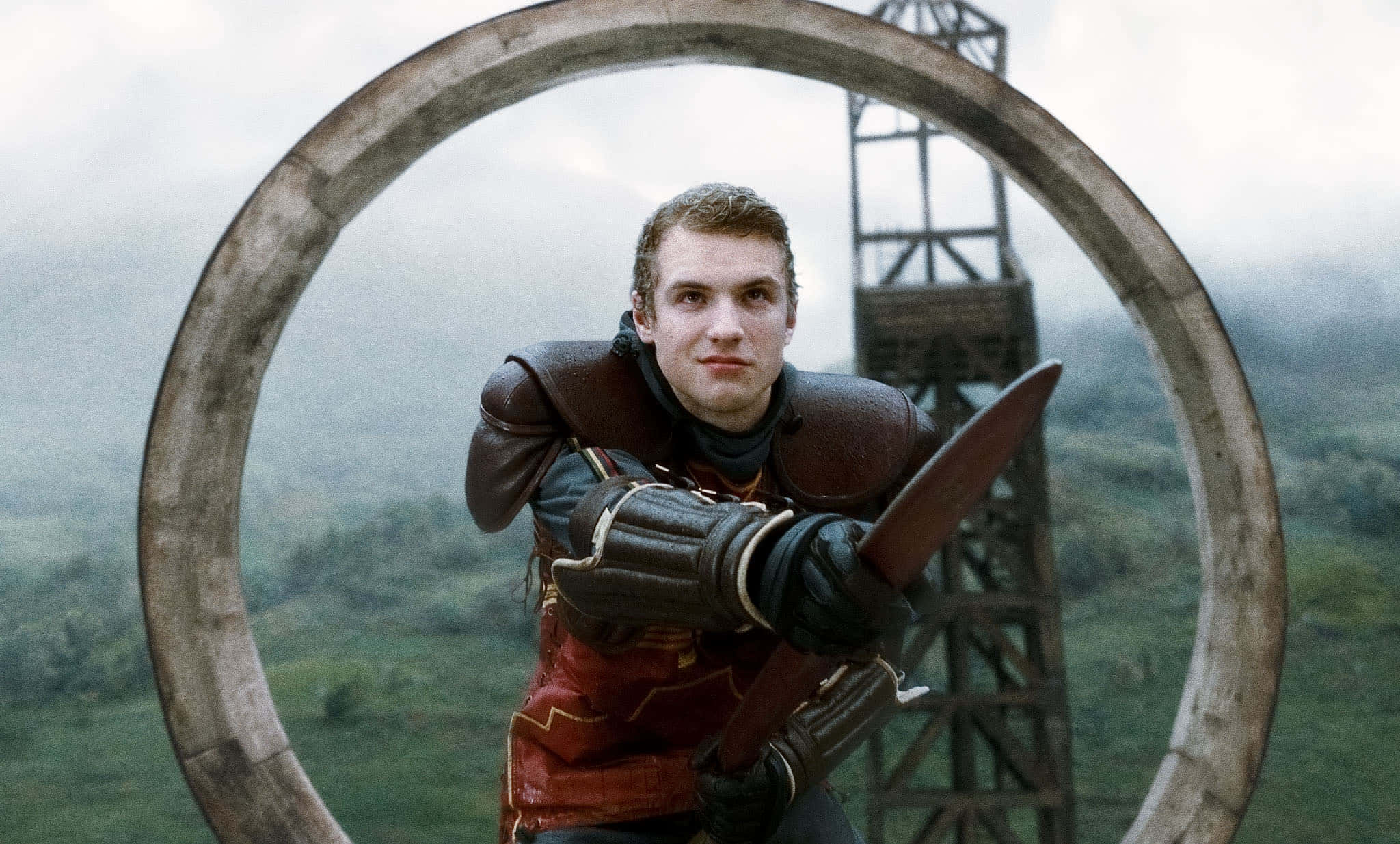 Quidditch 桌布 壁紙 — 一名身穿皮甲的戰士，手持利刃穿過一個巨大的石環，背景是霧氣瀰漫的綠色山谷。