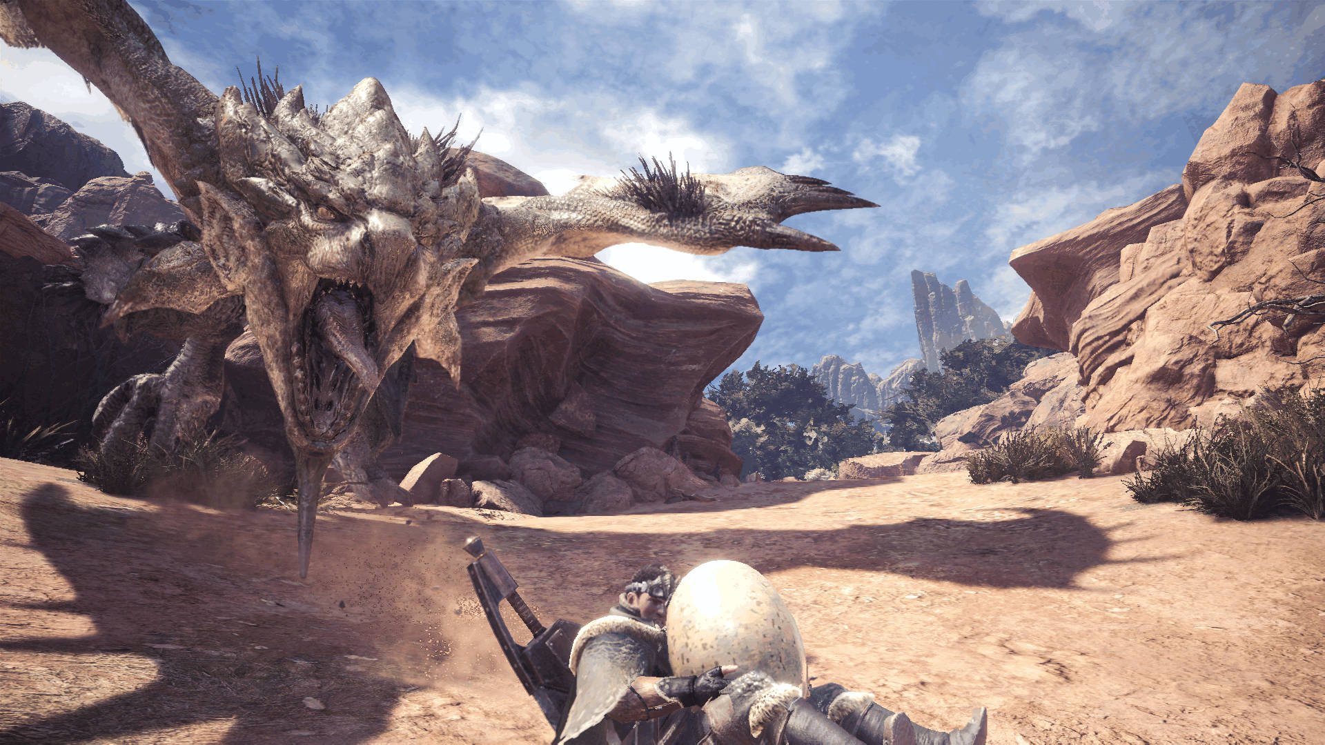 Monster Hunter World Iceborne 桌布 壁紙 — 一名身穿盔甲的獵人蹲在一個巨大的咆哮龍面前，身處陽光明媚的沙漠峽谷，有紅色岩層。