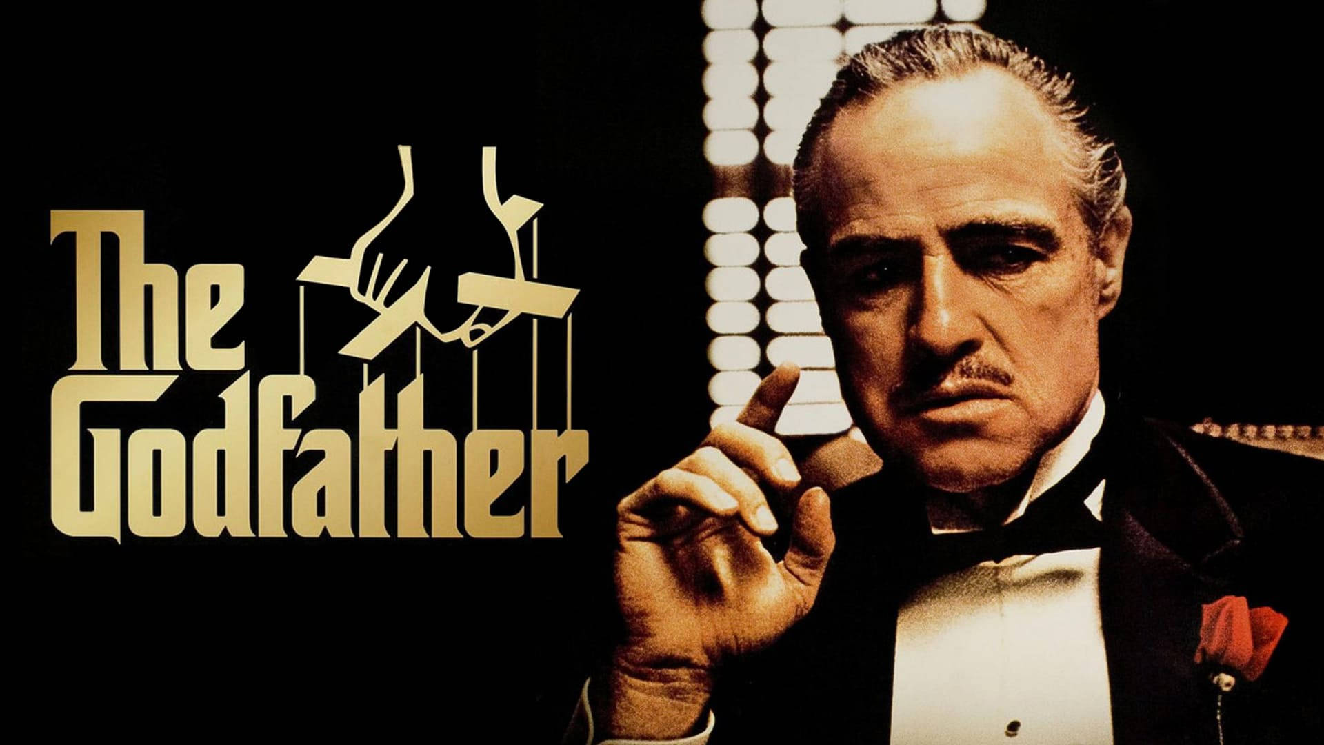 The Godfather 桌布 壁紙 — 一名身穿禮服、別著紅玫瑰胸針的男子舉起一根手指，而《教父》的標題在金色中閃耀，旁邊有一個木偶圖案。