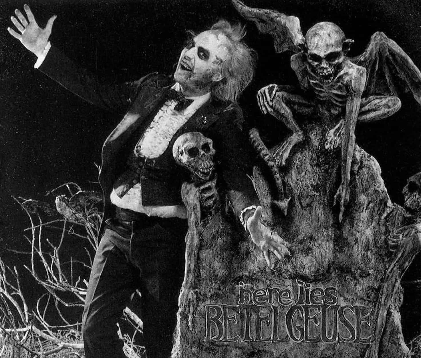 Beetlejuice 桌布 壁紙 — 一名身穿禮服、化著骷髏妝的男子站在墓碑旁，墓碑上有一隻骷髏蝙蝠生物，周圍是光禿禿的樹枝，形成鮮明的黑白場景。