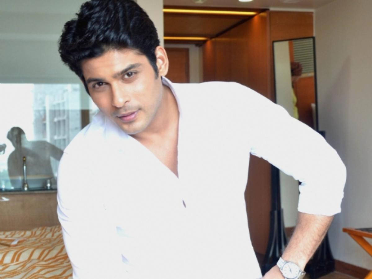 Sidharth Shukla 桌布 壁紙 — 一名身穿筆挺白襯衫的男子在現代酒店房間內自信地靠著，房間配有溫暖燈光和木質裝飾。