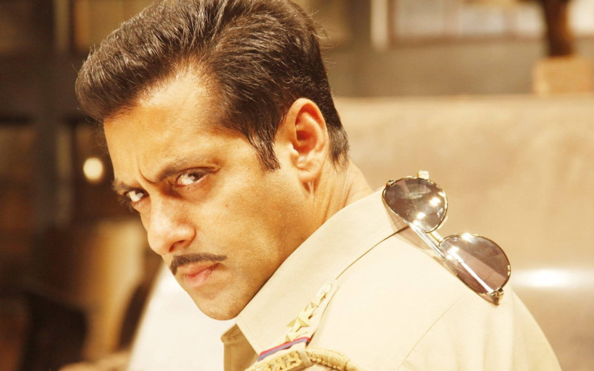 Salman Khan 桌布 壁紙 — 一名身穿米色制服、肩上掛著太陽眼鏡的男子，表情嚴肅地越過肩膀凝視著。