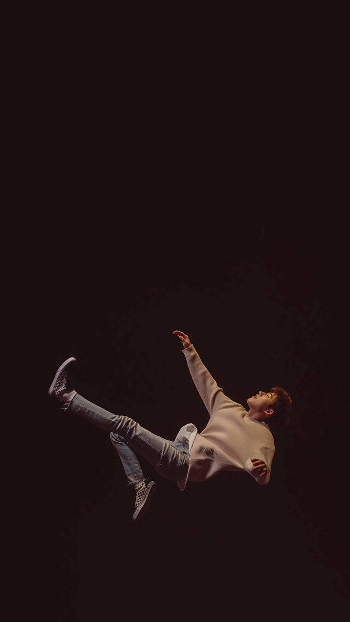 kim hanbin 桌布 壁紙 — 一名身穿米色毛衣和牛仔褲的年輕男子在黑暗背景下雙臂伸展，看似懸浮在半空中。