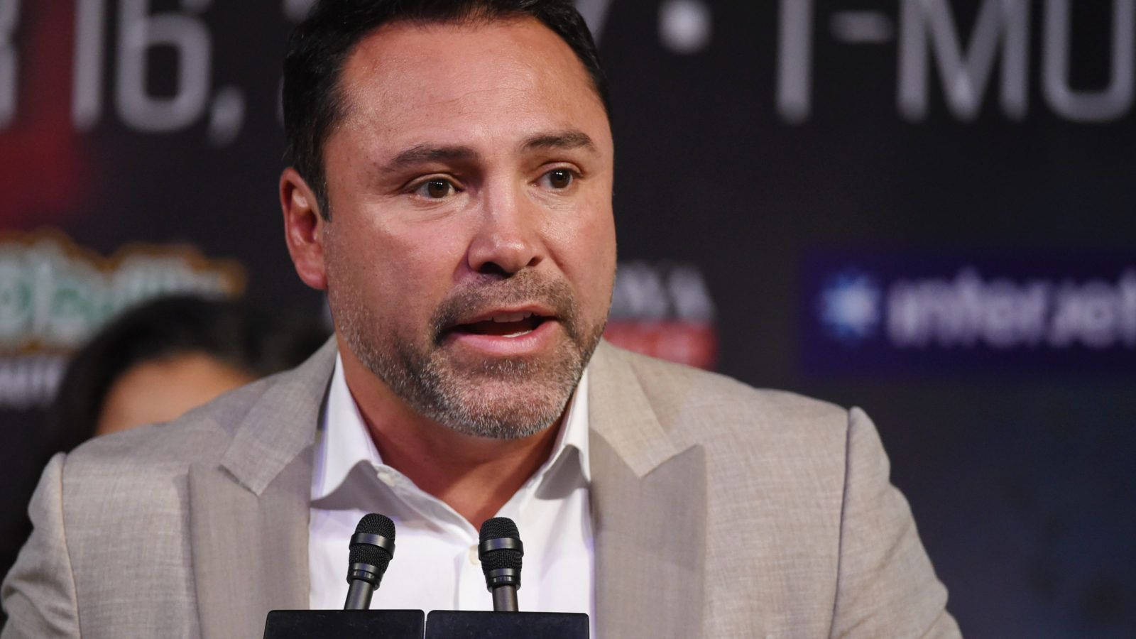 Boxing 桌布 壁紙 — 一名身穿米色西裝的男子在記者會上發言，身後有麥克風和品牌背景板。