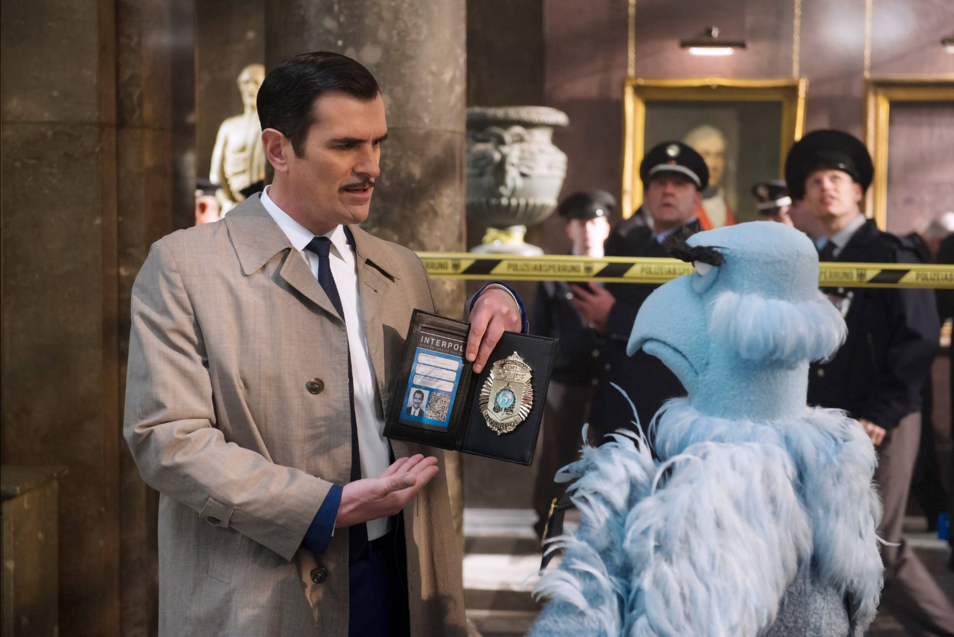 muppets 桌布 壁紙 — 一名身穿米色風衣的男子在一個有警察封條的大理石大廳中，向一隻藍色毛茸茸的生物出示INTERPOL證件。