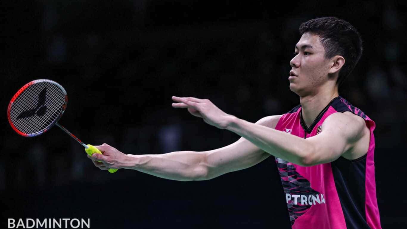 1366x768 Badminton 桌布 壁紙 — 一名身穿粉紅色和黑色球衣的男性羽球運動員在深色背景下揮動球拍擊打羽球。