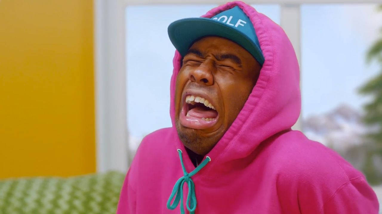 tyler 桌布 壁紙 — 一名身穿粉紅色連帽衫和青綠色帽子的男子在色彩繽紛的房間裡閉著眼睛尖叫。
