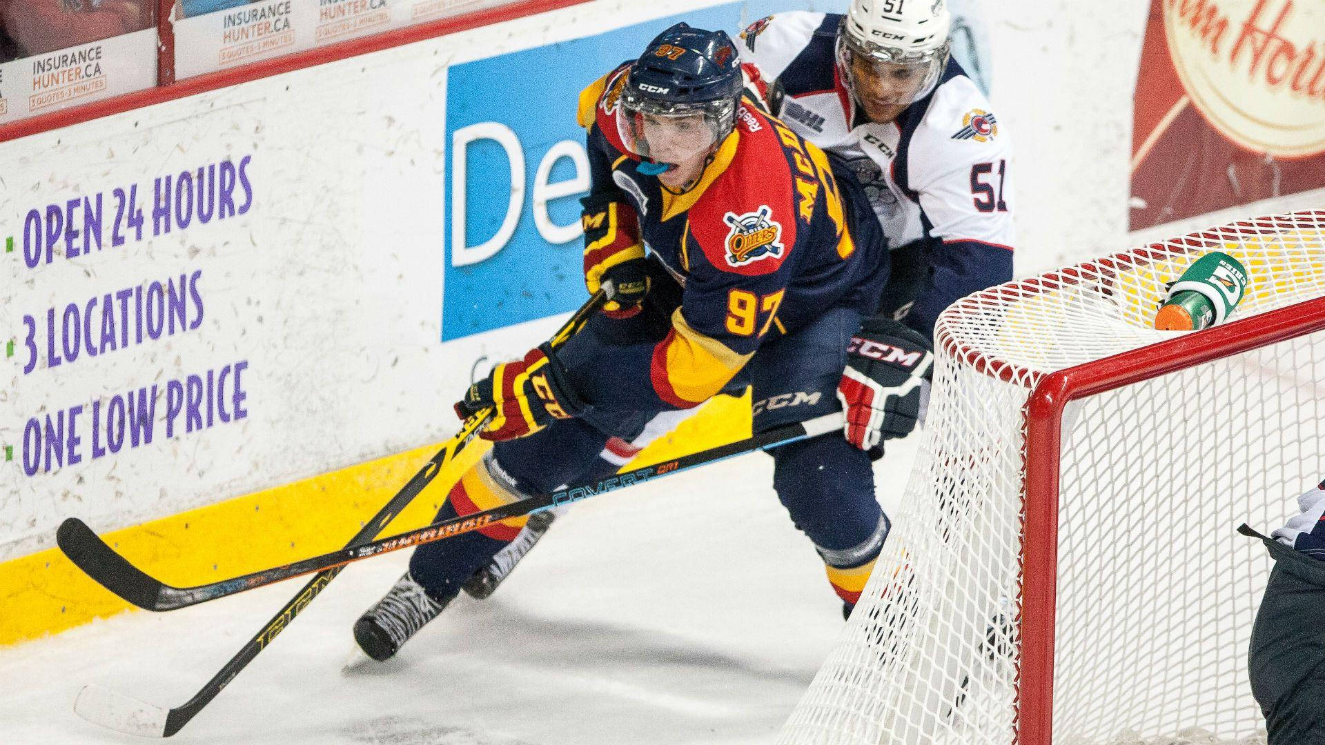 hockey 桌布 壁紙 — 一名身穿紅、黃、藍色球衣的冰球運動員在激烈比賽中於球門網附近爭奪冰球。