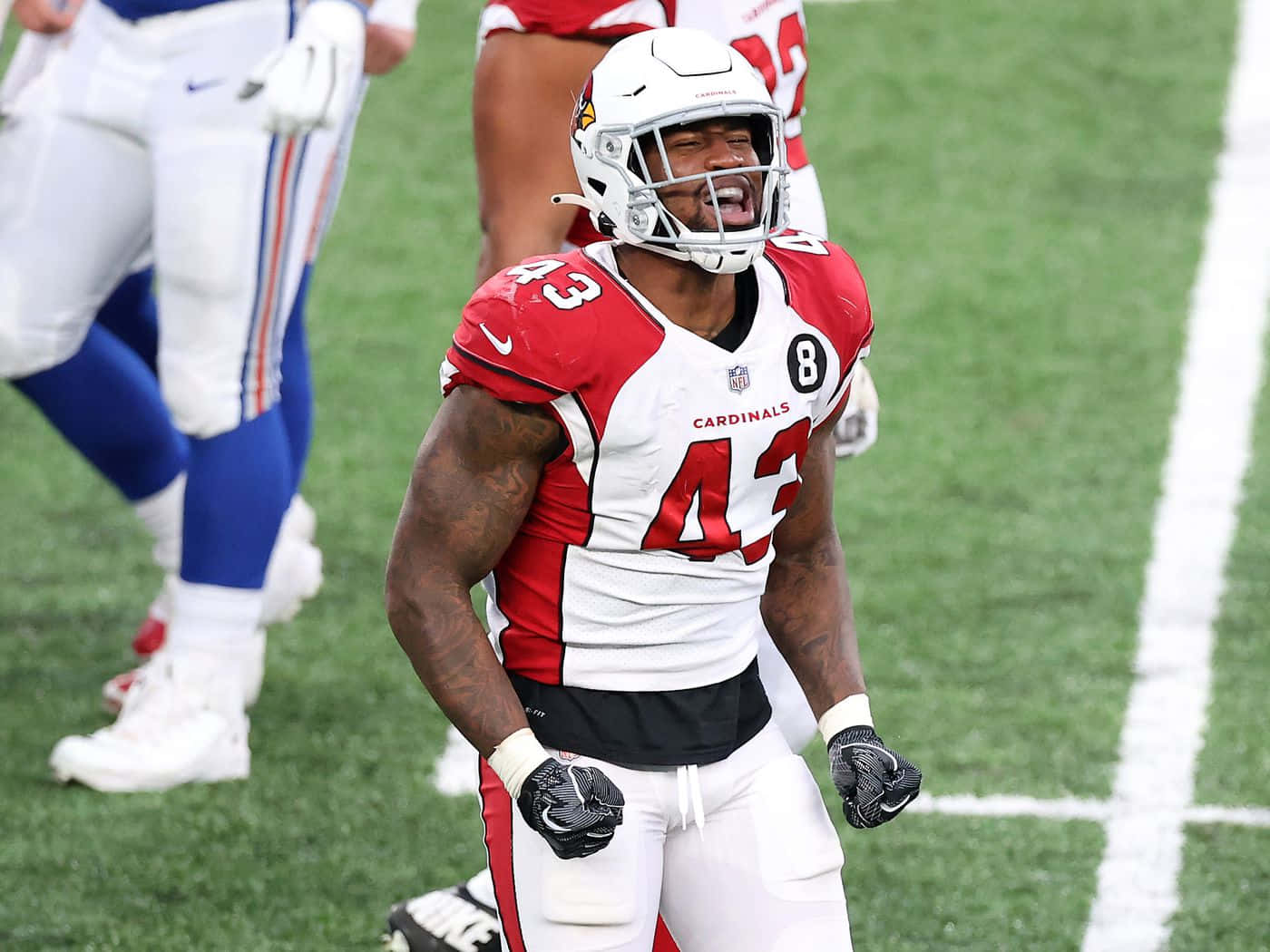 足球 桌布 壁紙 — 一名身穿紅白 Cardinals 裝備的美式足球員在帶有白色碼線的綠色球場上慶祝。
