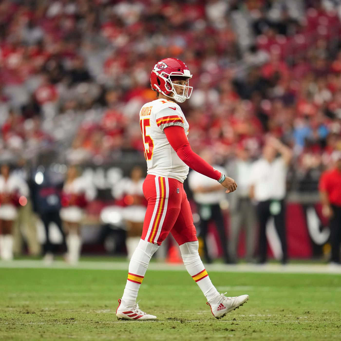 Kansas City Chiefs 4K 桌布 壁紙 — 一名身穿紅白球衣的堪薩斯城酋長隊四分衛走過綠色球場，身後體育場人群模糊。