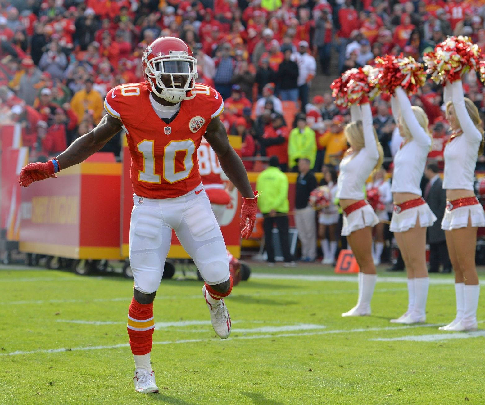 Tyreek Hill 桌布 壁紙 — 一名身穿紅白球衣的堪薩斯城酋長隊美式足球員在陽光明媚的綠色球場上慶祝，身後有啦啦隊和座無虛席的體育場。