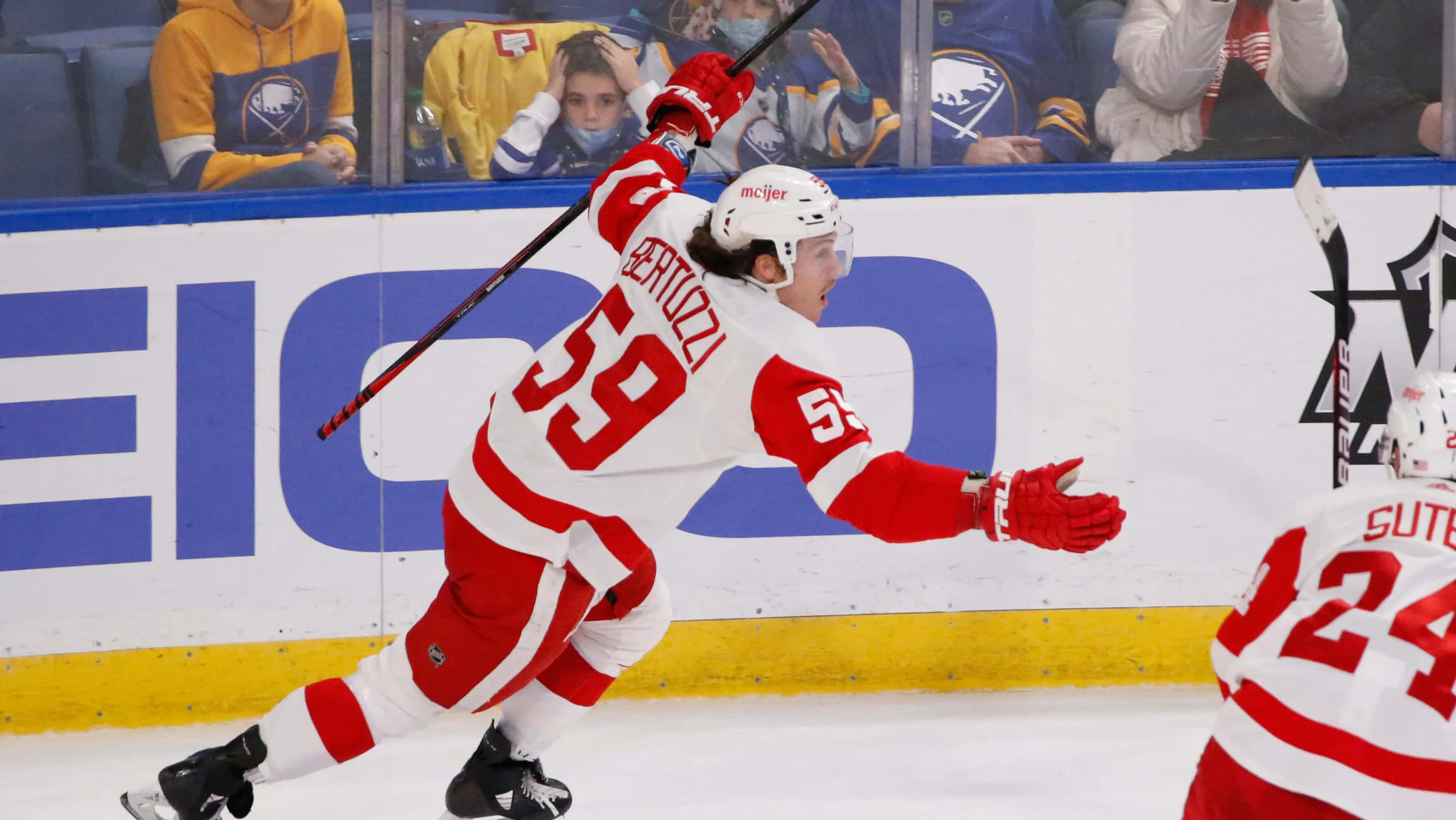 Tyler Bertuzzi 桌布 壁紙 — 一名身穿紅白球衣的曲棍球運動員在冰上高舉雙臂和球棍慶祝進球。