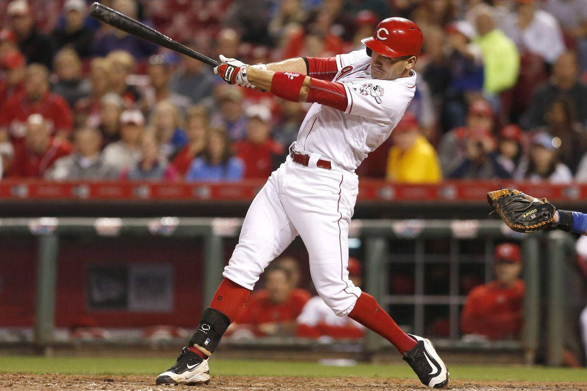 Joey Votto 桌布 壁紙 — 一名身穿紅白球衣的棒球選手在夜間比賽中揮棒，背景有模糊的人群。