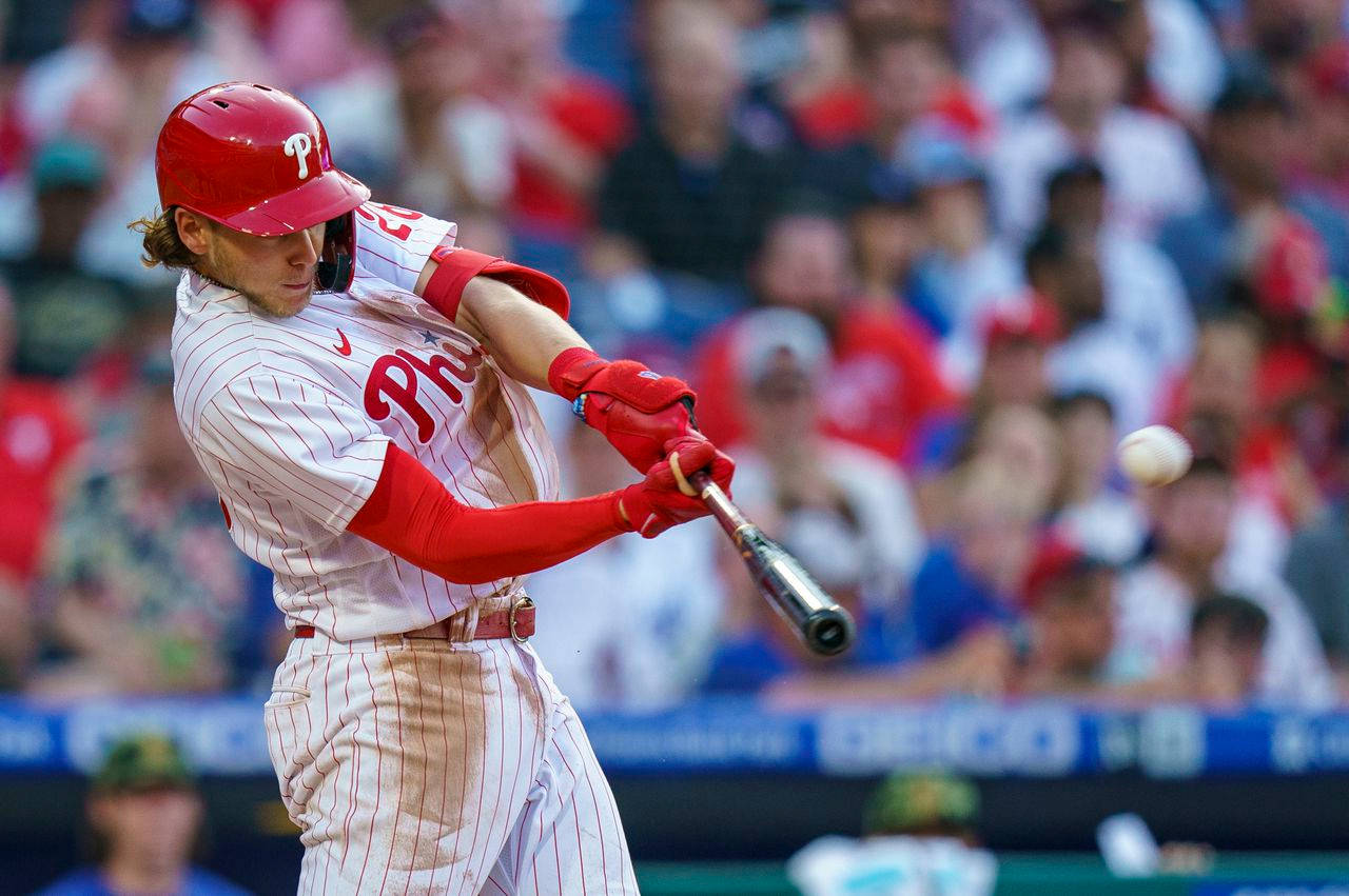 Phillies 桌布 壁紙 — 一名身穿紅白球衣的棒球選手在日間比賽中揮棒擊球，背景有模糊的人群。