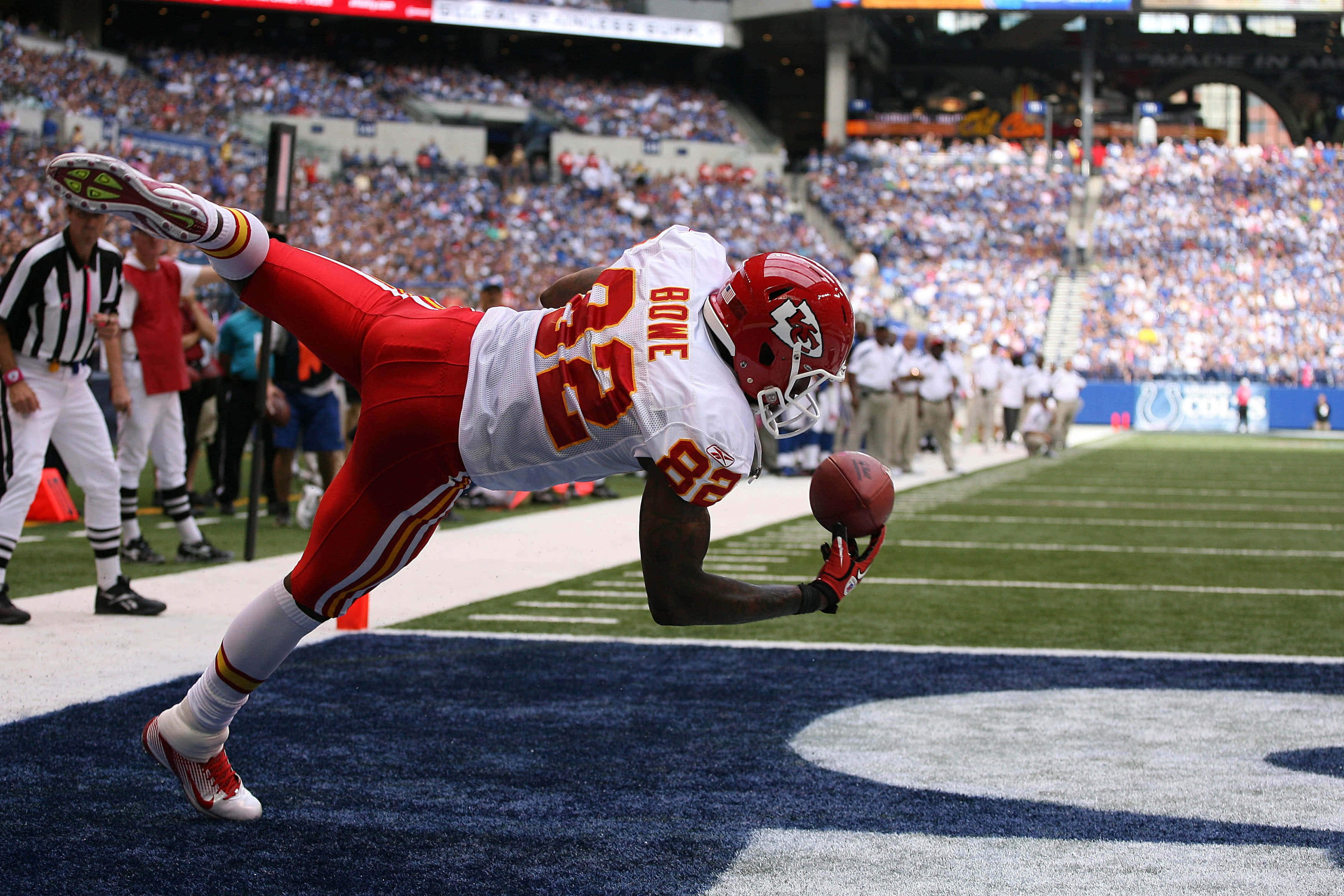 Kansas City Chiefs 4K 桌布 壁紙 — 一名身穿紅白球衣的美式足球員在半空中飛撲，在端區附近接球，身後是座無虛席的體育場。