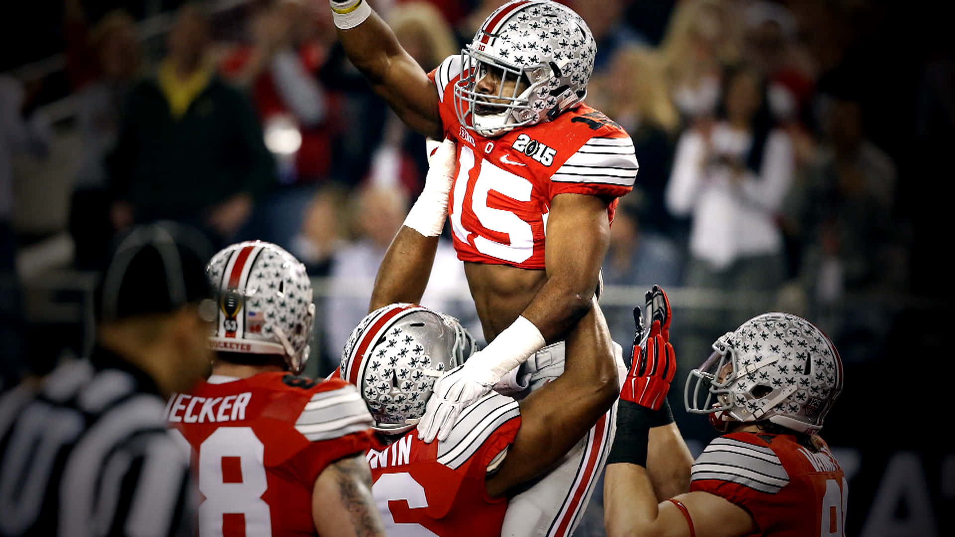 Cool Ohio State 桌布 壁紙 — 一名身穿紅白球衣的足球員在明亮燈光下的體育場中被隊友抬起慶祝。