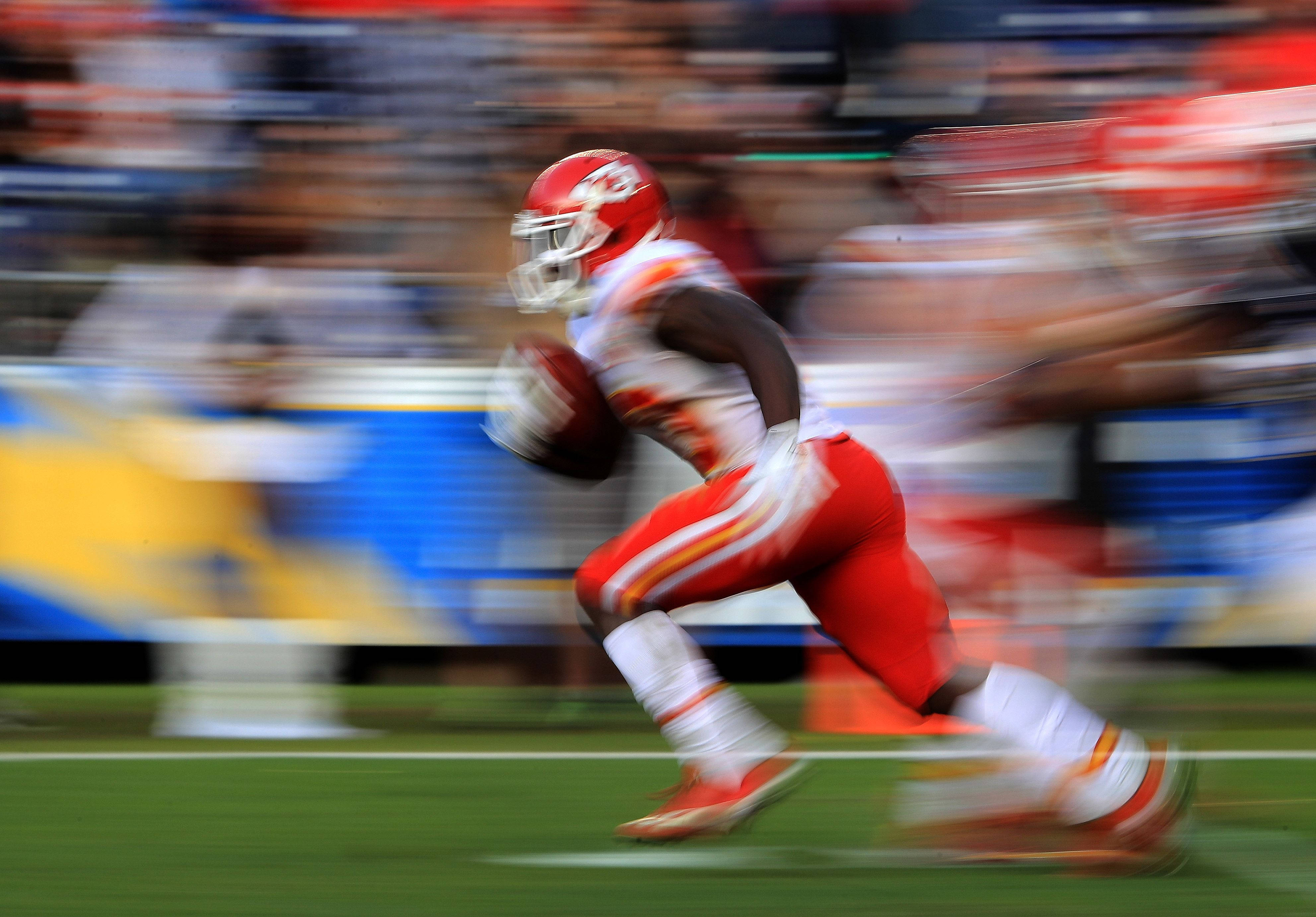 Tyreek Hill 桌布 壁紙 — 一名身穿紅白球衣的足球員帶著球在模糊的球場上衝刺。