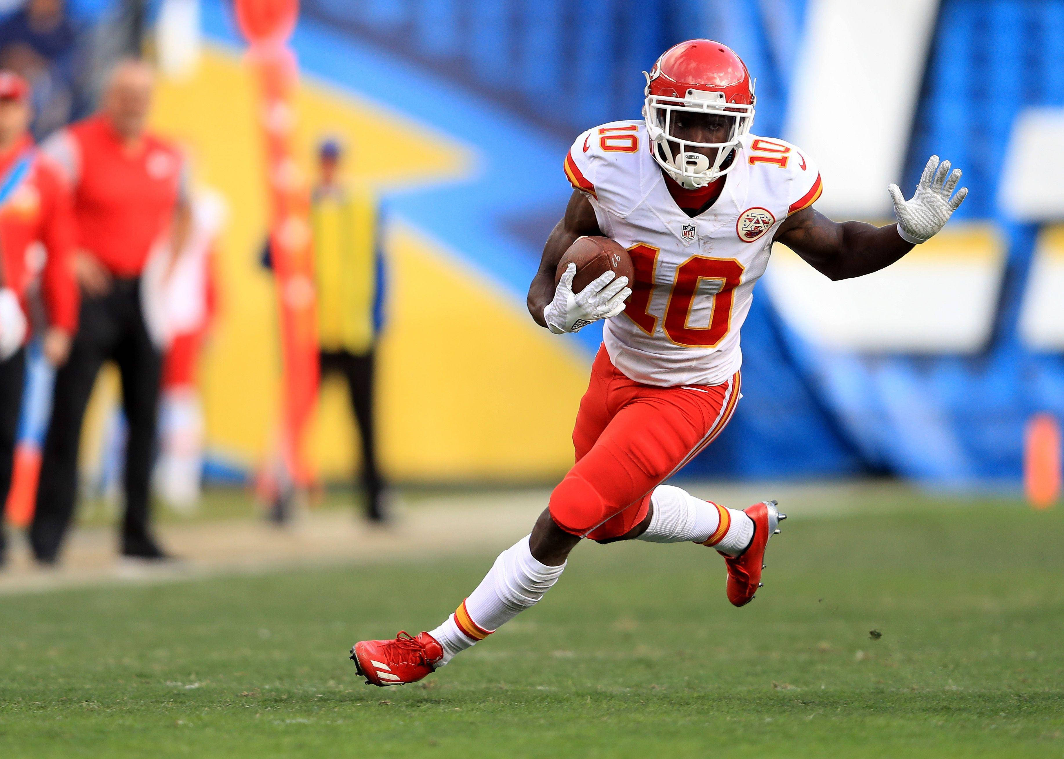 Tyreek Hill 桌布 壁紙 — 一名身穿紅白球衣的足球運動員，帶著專注的強度，在綠色球場上持球衝刺。