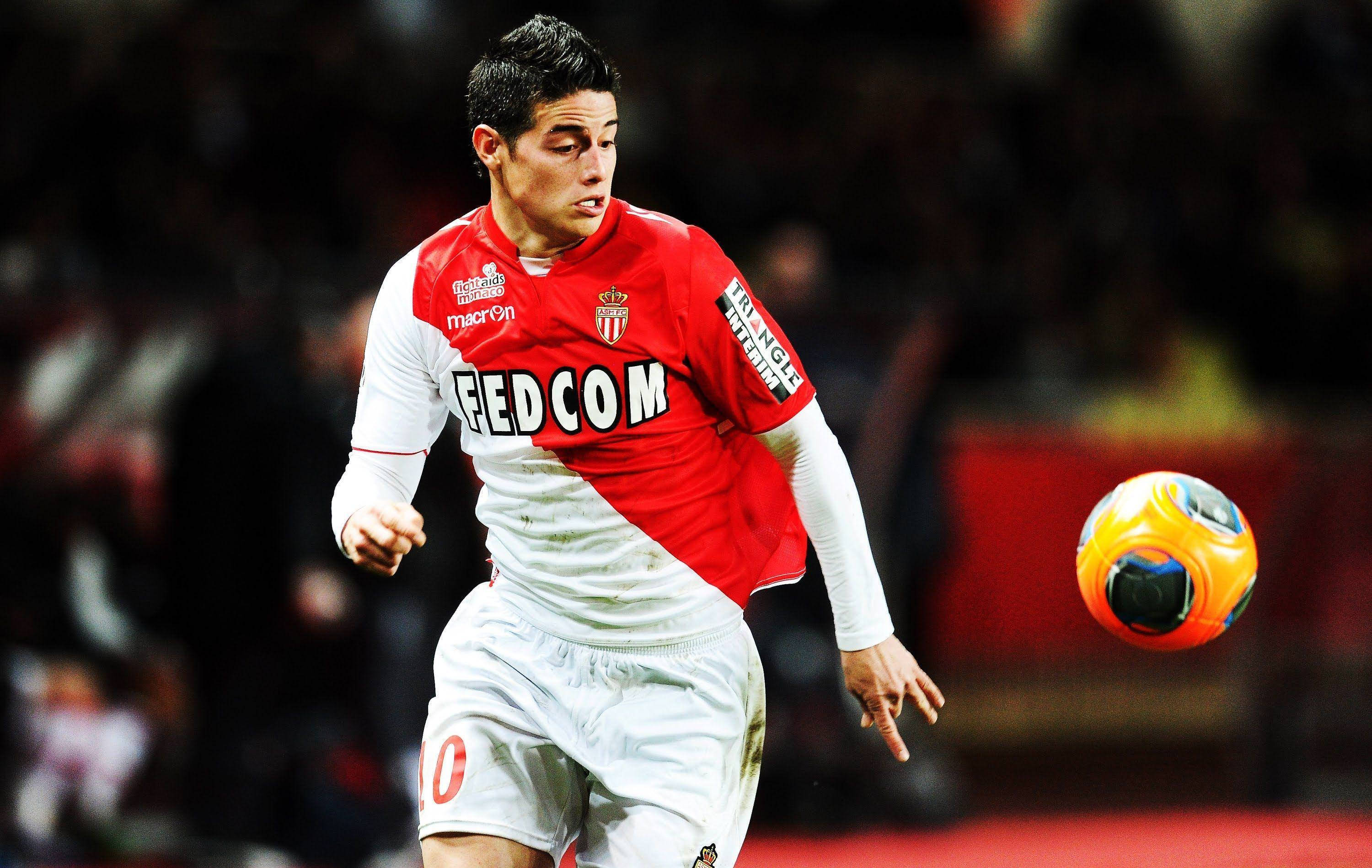 James Rodriguez 桌布 壁紙 — 一名身穿紅白球衣的足球運動員在夜間比賽中，在球場燈光下盤帶一個色彩繽紛的球。
