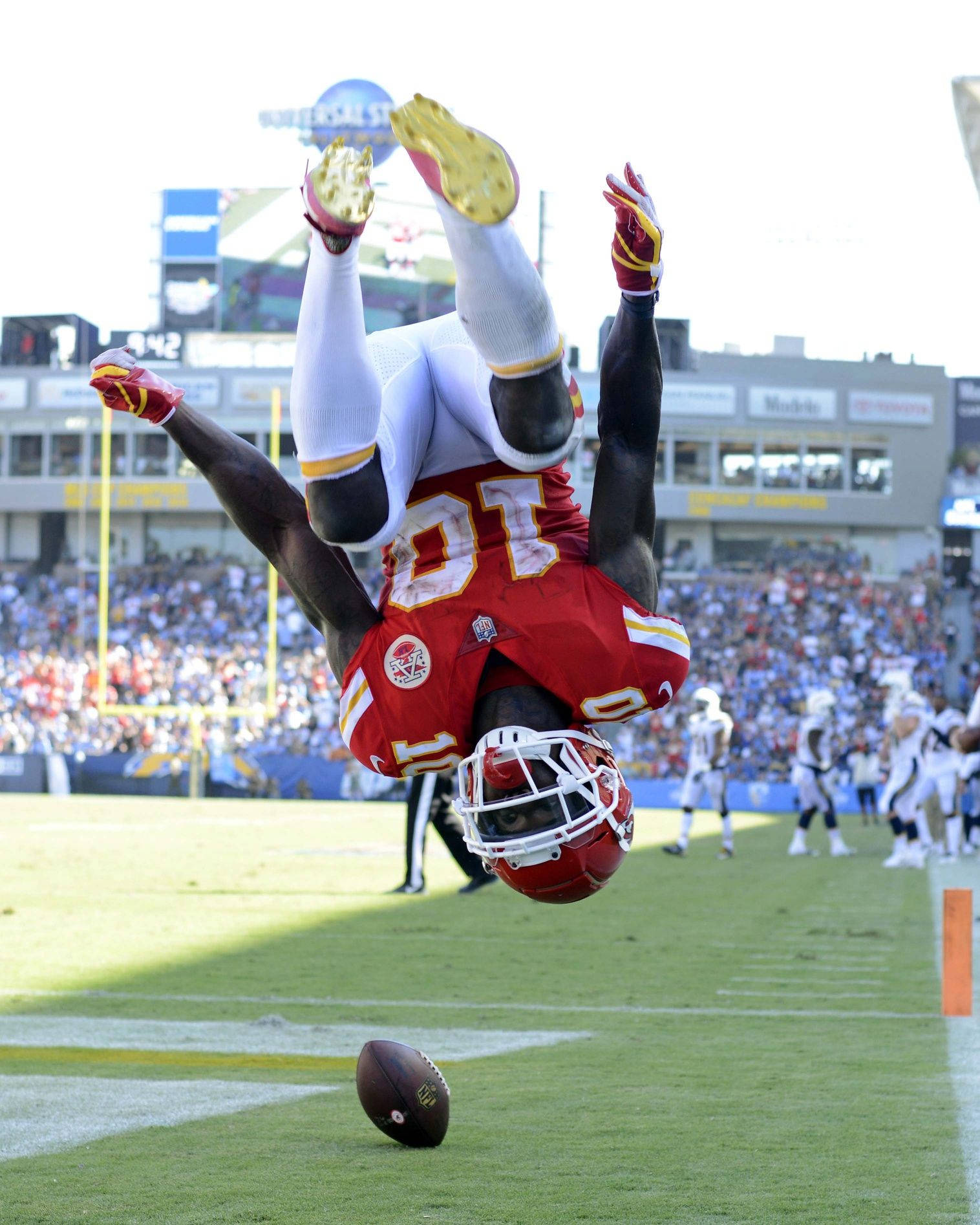 Tyreek Hill 桌布 壁紙 — 一名身穿紅白球衣的足球運動員在陽光明媚的球場上，於足球上方做出空中翻騰的特技動作。