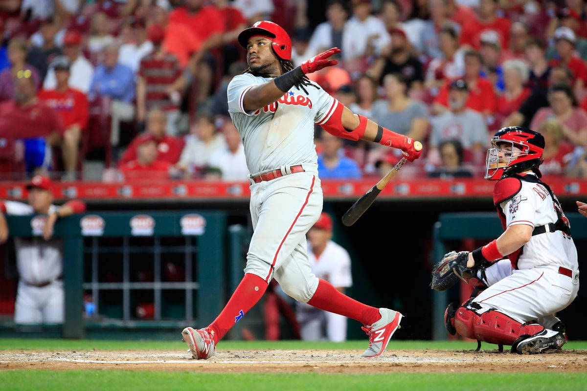 Phillies 桌布 壁紙 — 一名身穿紅白色球衣的棒球選手在本壘板揮棒，捕手蹲在他身後，周圍是體育場的人群。