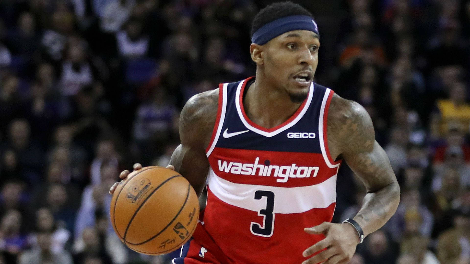 Bradley Beal 桌布 壁紙 — 一名身穿紅白藍華盛頓球衣的籃球運動員在比賽中激烈運球，身後是模糊的人群。