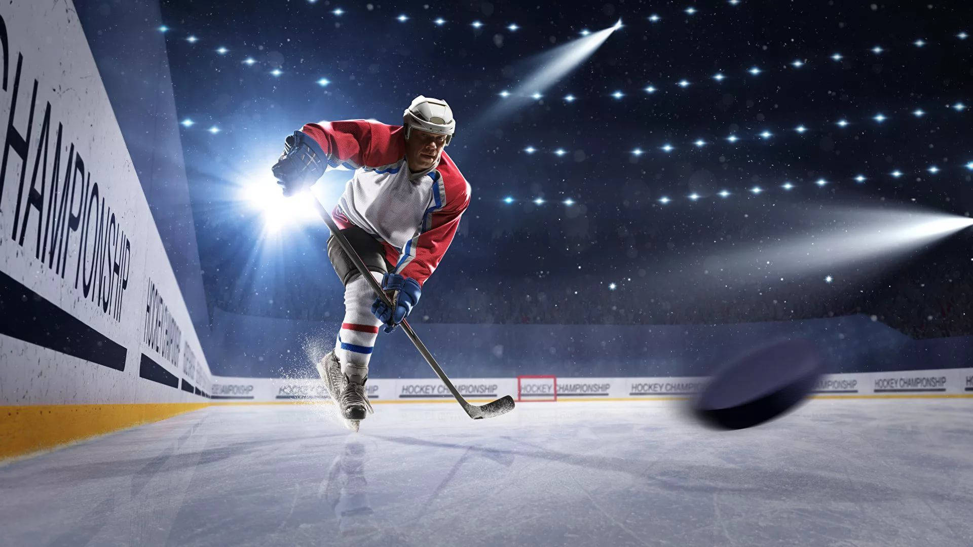 hockey 桌布 壁紙 — 一名身穿紅白裝備的冰球運動員在明亮的場館燈光下在冰上激烈滑行追逐冰球。