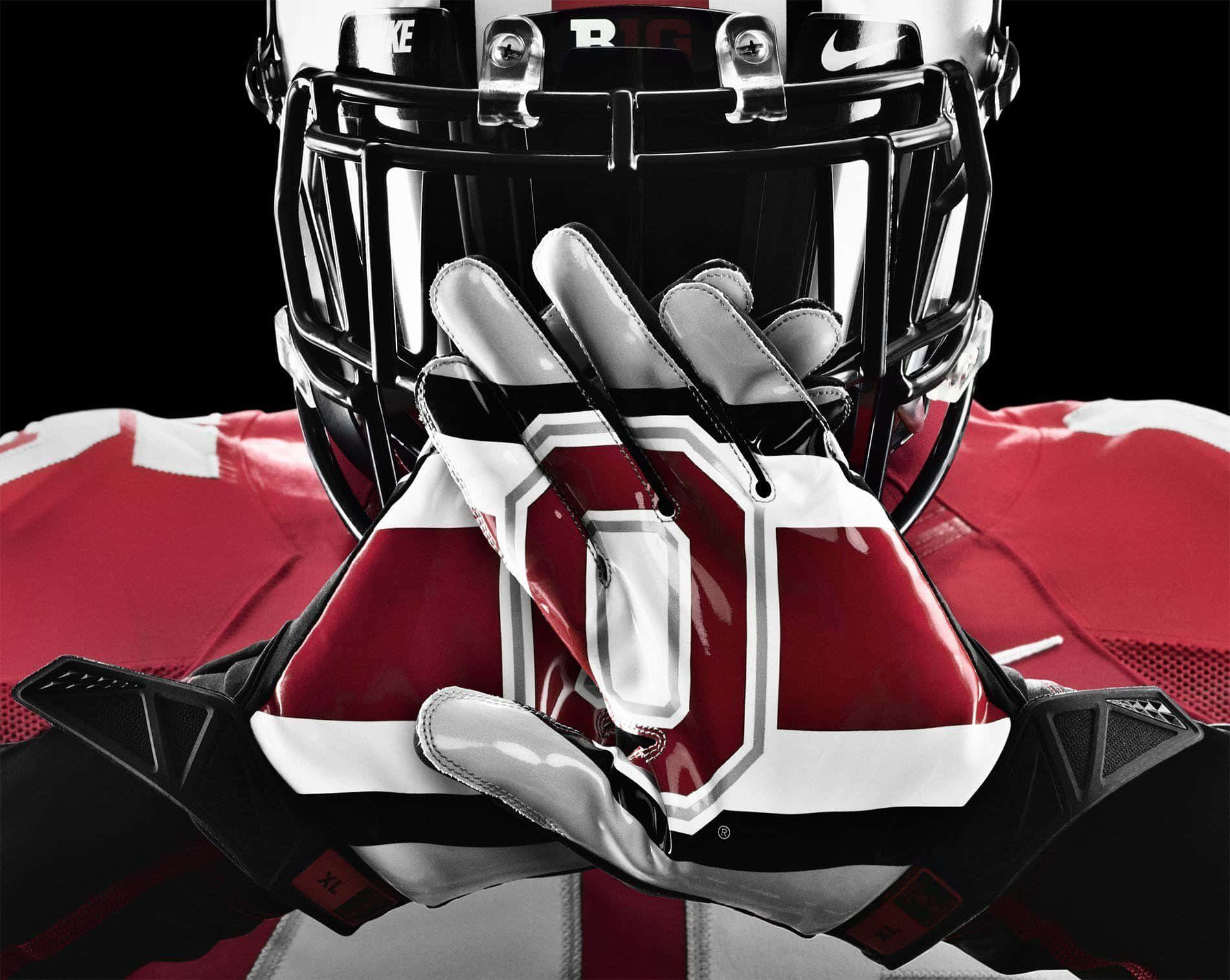 Ohio State Football 桌布 壁紙 — 一名身穿紅白裝備的美式足球員，戴著手套的雙手捧著頭盔，背景為黑色。