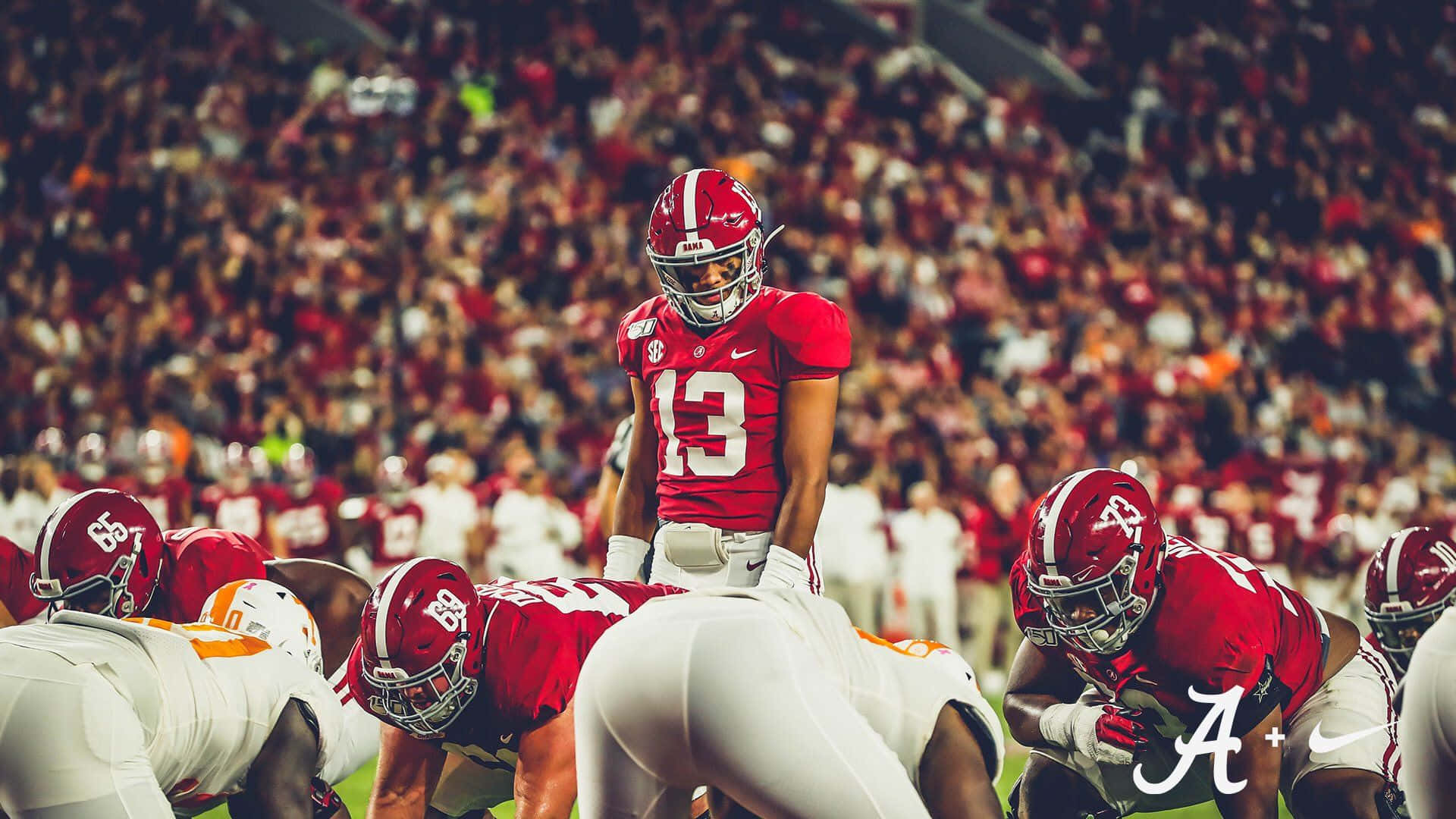 Tua Tagovailoa 桌布 壁紙 — 一名身穿紅色13號球衣的美式足球員在夜間比賽中，於球場燈光下站在爭球線上蓄勢待發。