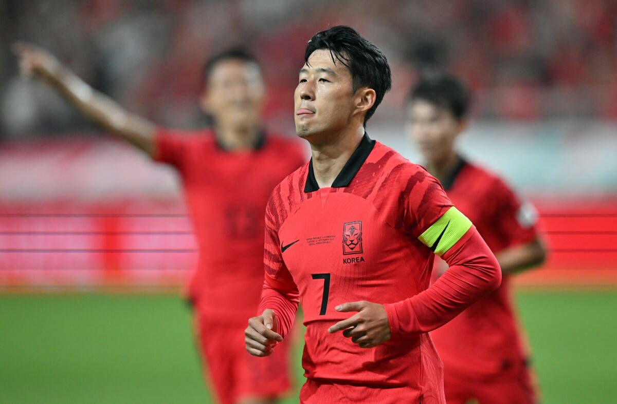 Football Players 桌布 壁紙 — 一名身穿紅色7號球衣的南韓足球員在綠色球場上奔跑，背景有模糊的隊友。