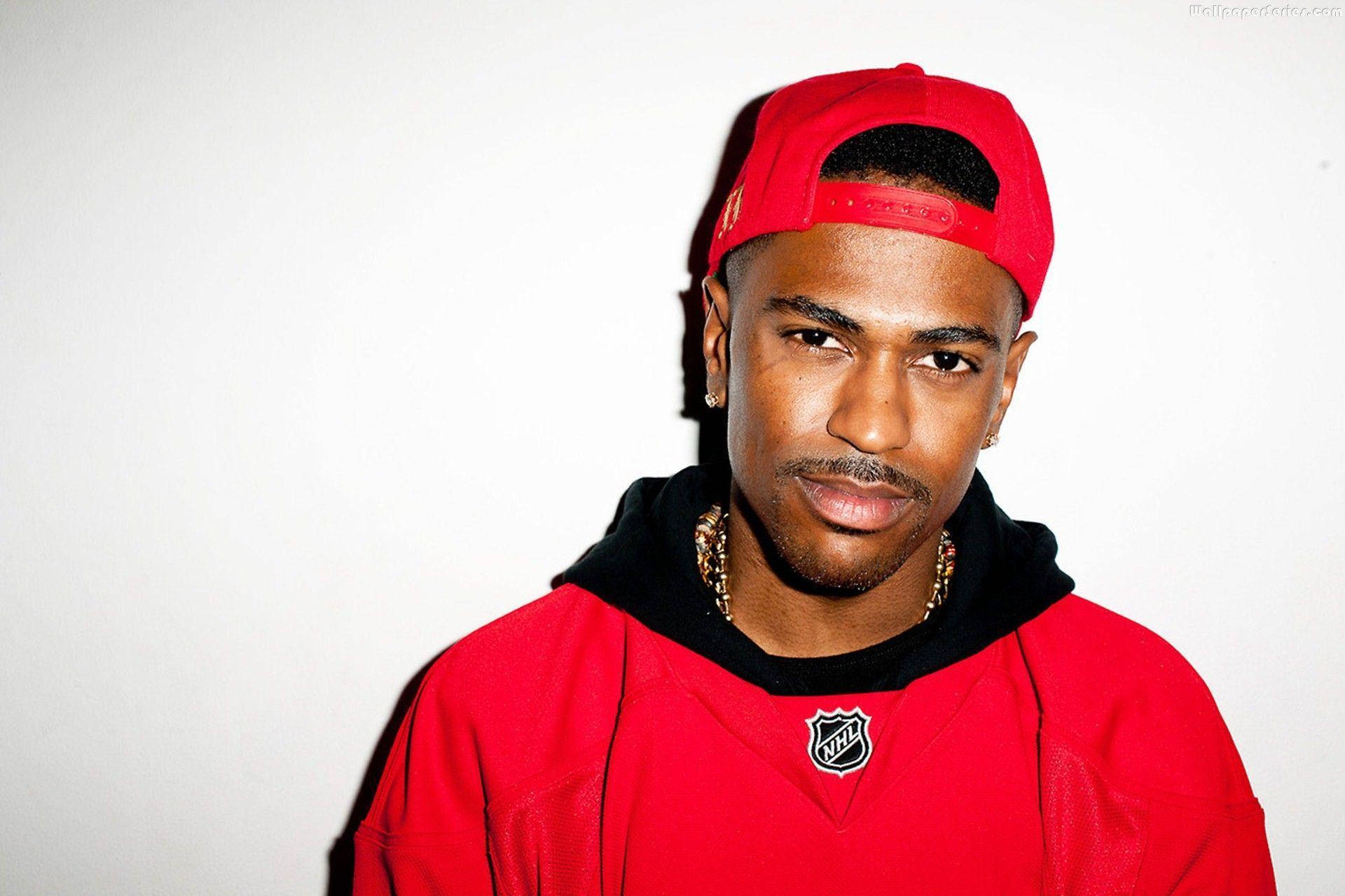 Big Sean 桌布 壁紙 — 一名身穿紅色NHL球衣和帽子的年輕男子，在純白色背景上帶有戲劇性陰影，自信地凝視著。