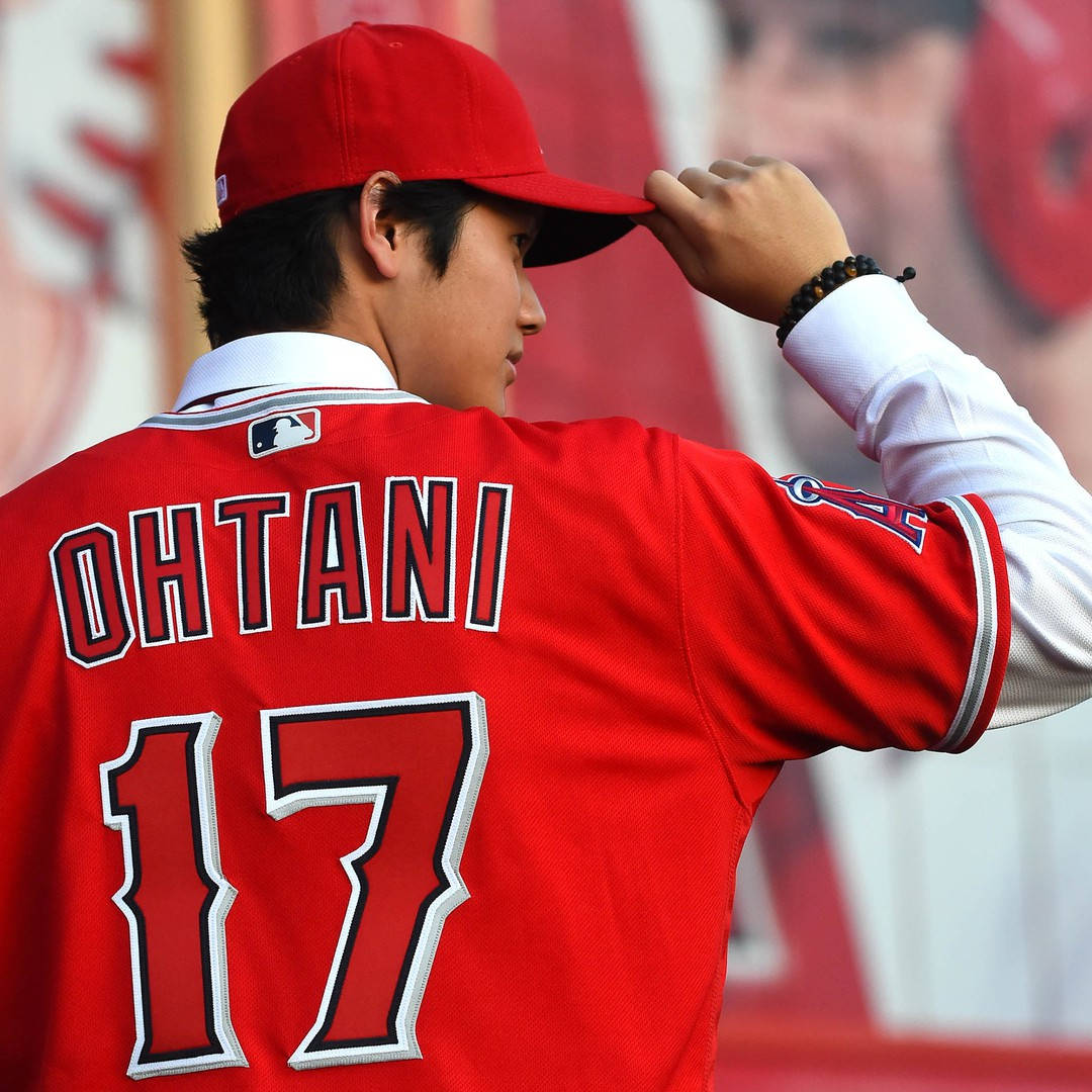 白色 桌布 壁紙 — 一名身穿紅色Ohtani 17號球衣的棒球運動員站在球場上調整帽子。