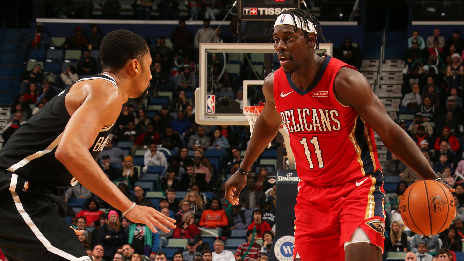 Jrue Holiday 桌布 壁紙 — 一名身穿紅色Pelicans球衣的籃球運動員在比賽中運球，同時被一名身穿黑白球衣的對手防守。