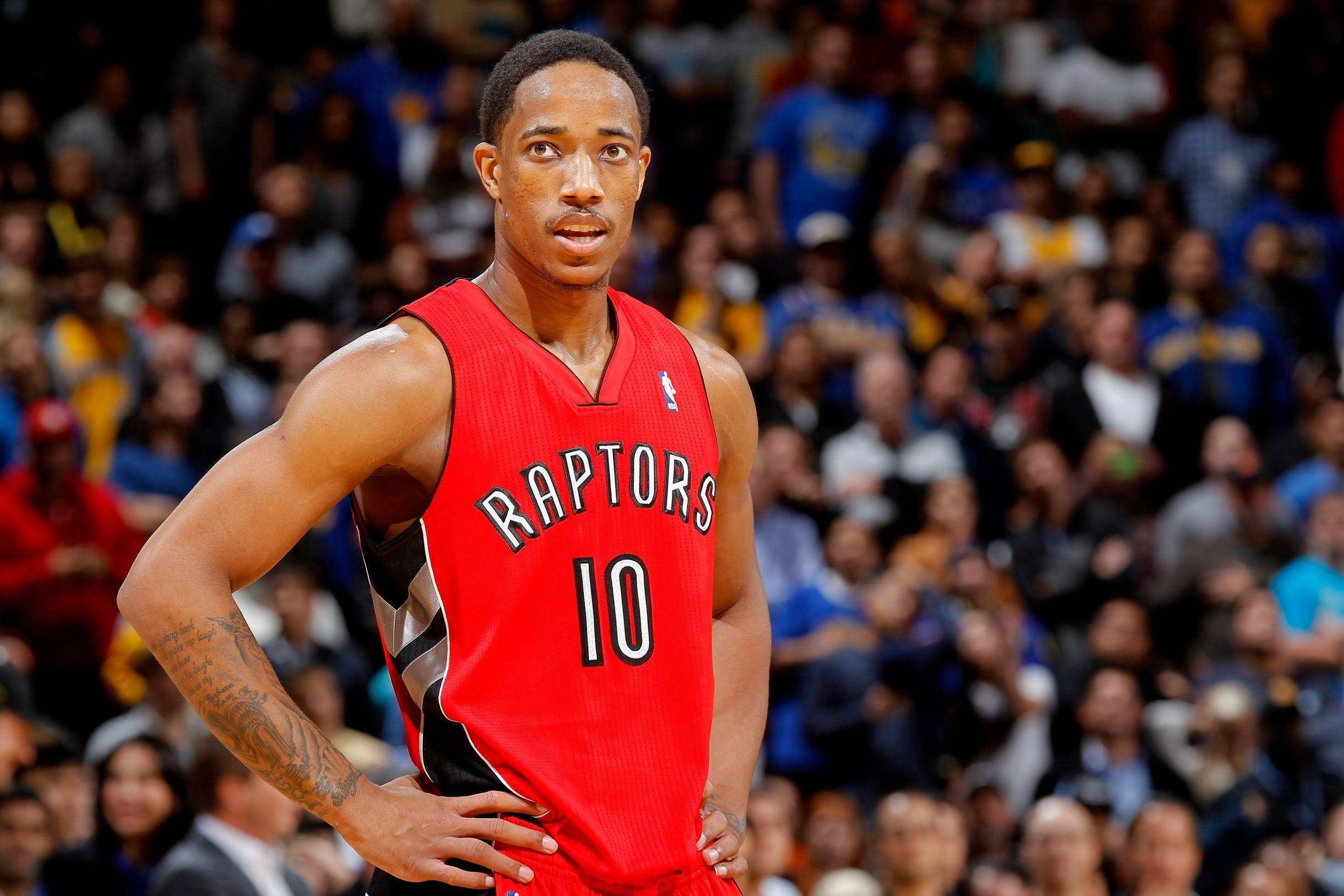 NBA 桌布 壁紙 — 一名身穿紅色Raptors球衣的籃球運動員在比賽中自信地雙手叉腰站立，身後是模糊的人群。