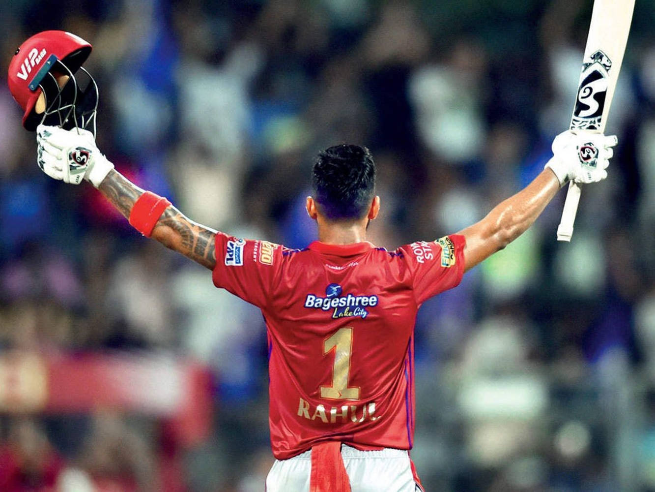 kl rahul 桌布 壁紙 — 一名身穿紅色一號球衣的板球運動員在夜間球場高舉球棒和頭盔，擺出勝利姿勢。