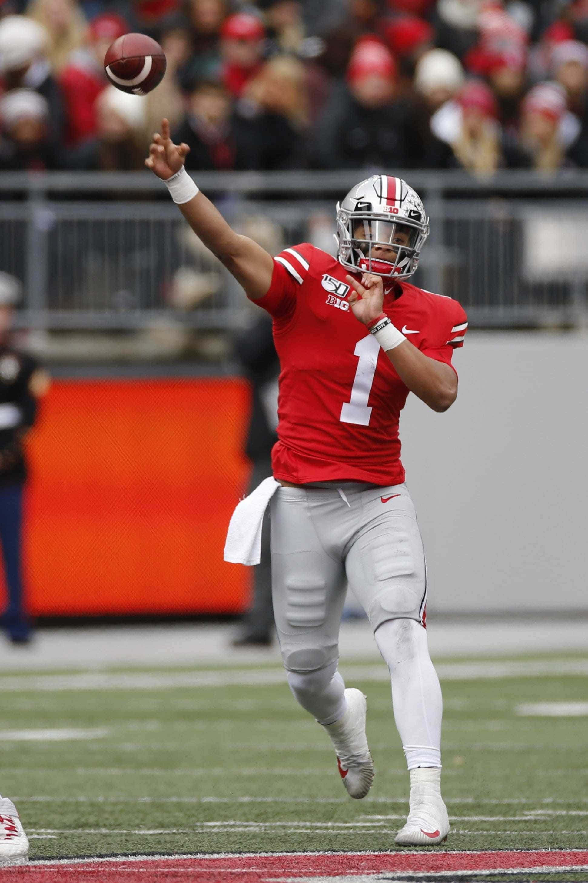 Justin Fields 桌布 壁紙 — 一名身穿紅色一號球衣的美式足球四分衛在綠色球場上空中傳球，背景有模糊的觀眾。
