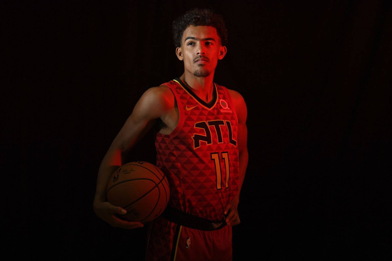 Trae Young 桌布 壁紙 — 一名身穿紅色亞特蘭大球衣的籃球運動員在黑色背景前，在戲劇性的紅色燈光下持球。