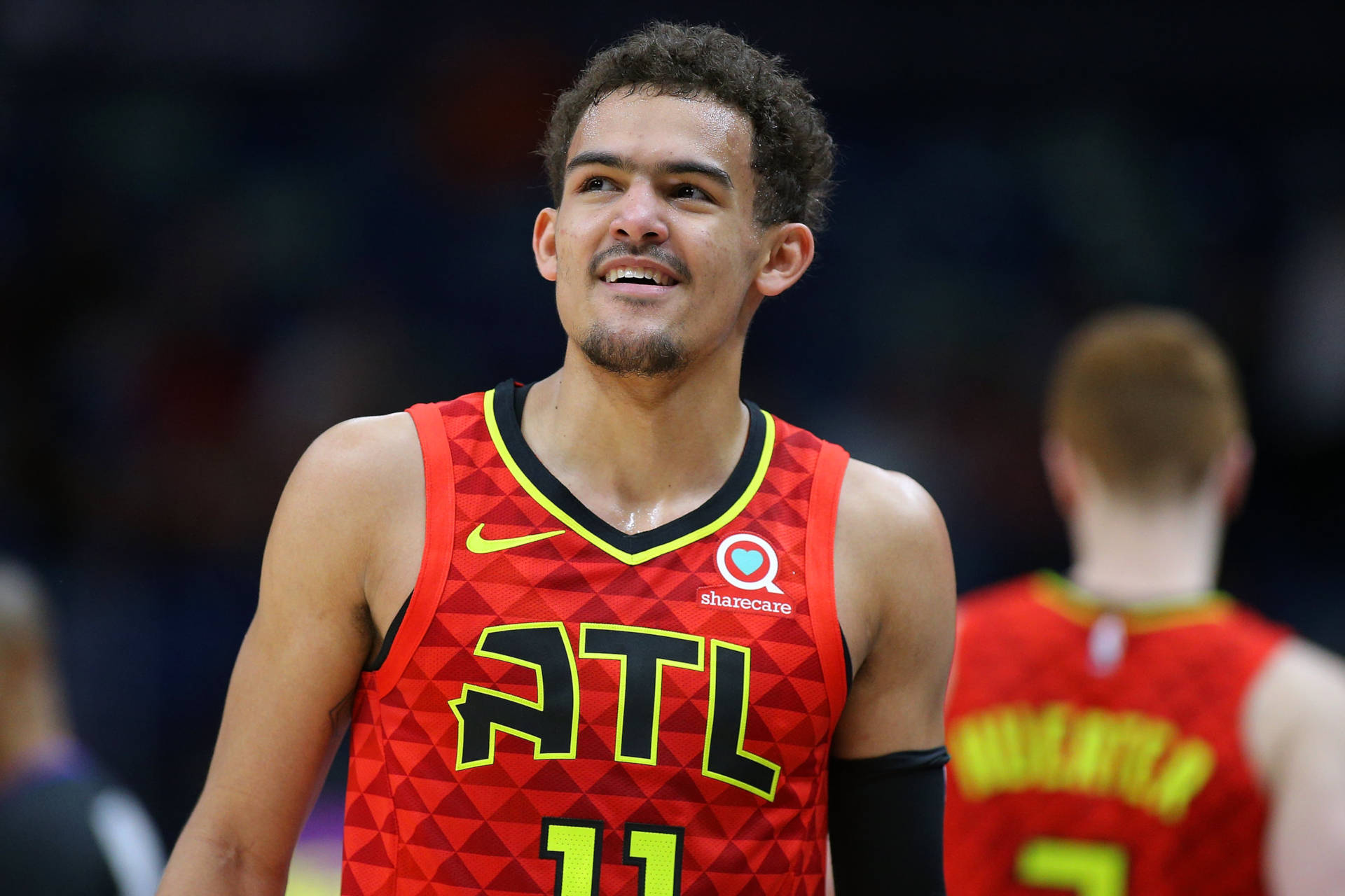 Trae Young 桌布 壁紙 — 一名身穿紅色亞特蘭大老鷹隊球衣的籃球運動員在比賽中微笑，身後可見隊友。